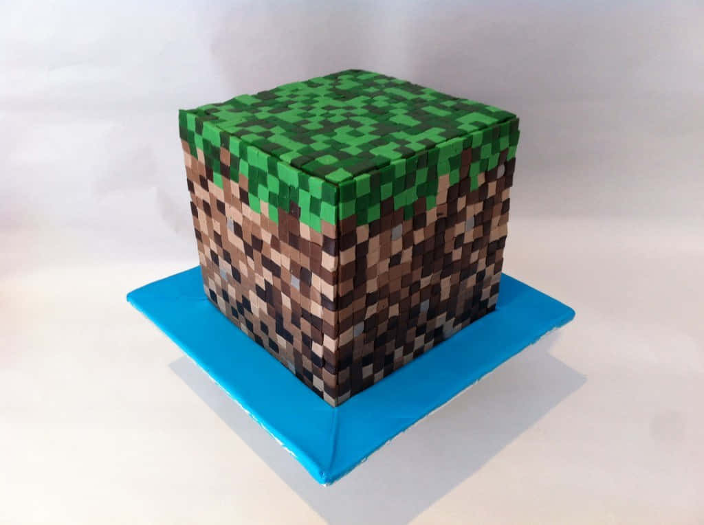 Minecraft Cakes 桌布 壁紙 — 一個像素化的Minecraft草地磚蛋糕，帶有棕色泥土紋理，放在白色背景的藍色底座上。