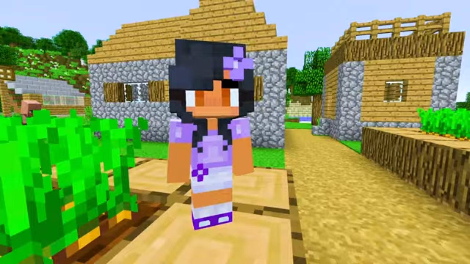Aphmau 桌布 壁紙 — 一個像素化的Minecraft角色，紫色頭髮和服裝，站在一條泥路上，附近有石頭和木頭建造的房屋，周圍有綠色灌木。