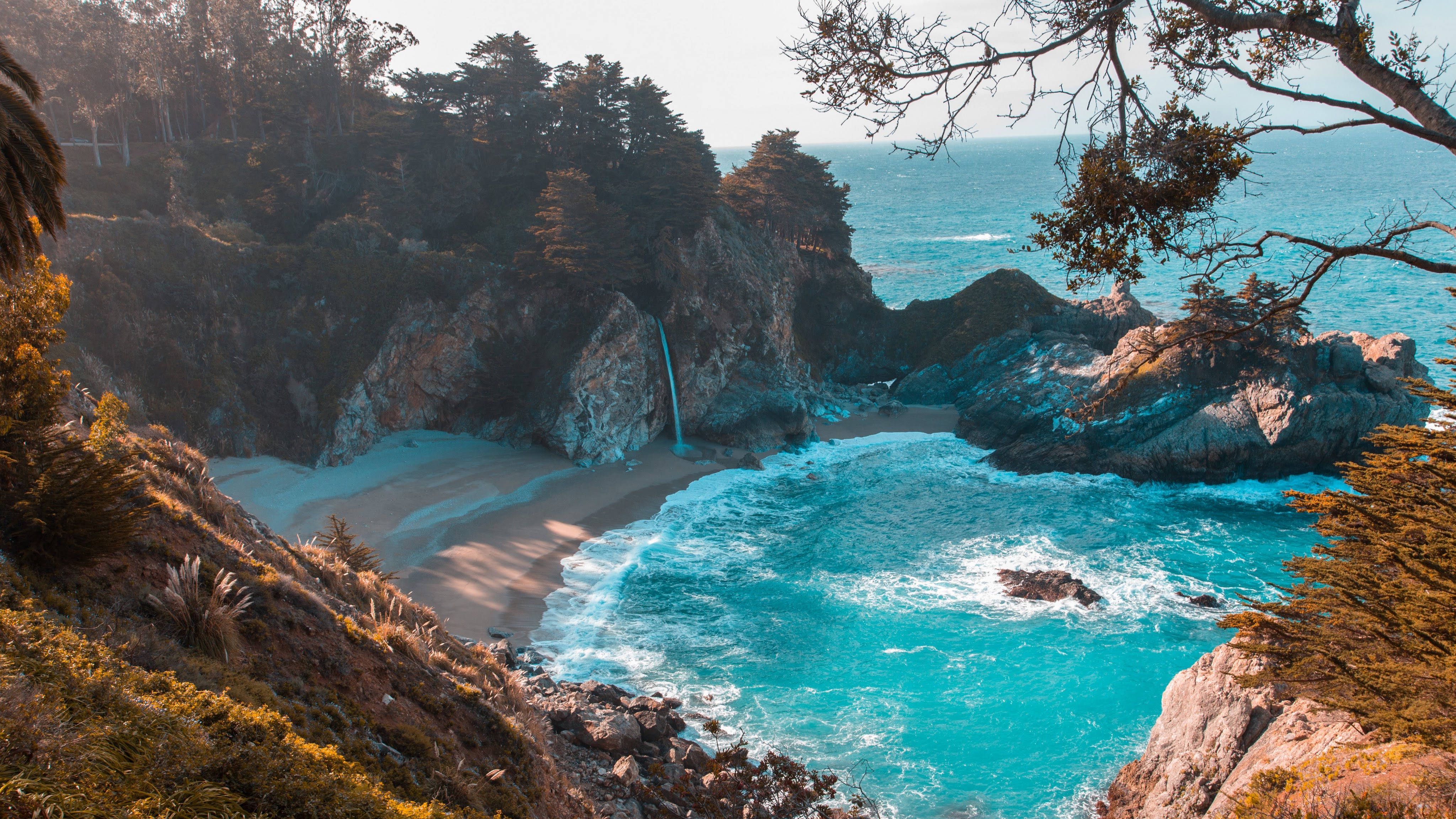 山景 桌布 壁紙 — 一個僻靜的小海灣，碧綠色的海浪拍打著沙灘，沙灘兩旁是崎嶇的懸崖和海岸樹木。