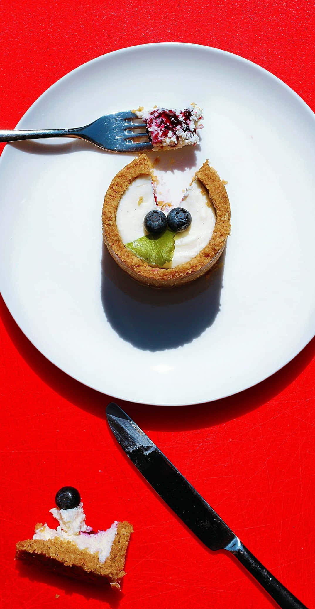 Pixel 3 Desserts 桌布 壁紙 — 一個充滿奇思妙想的迷你塔，上面有藍莓和奇異果，放在白色盤子上，襯托著大膽的紅色背景。