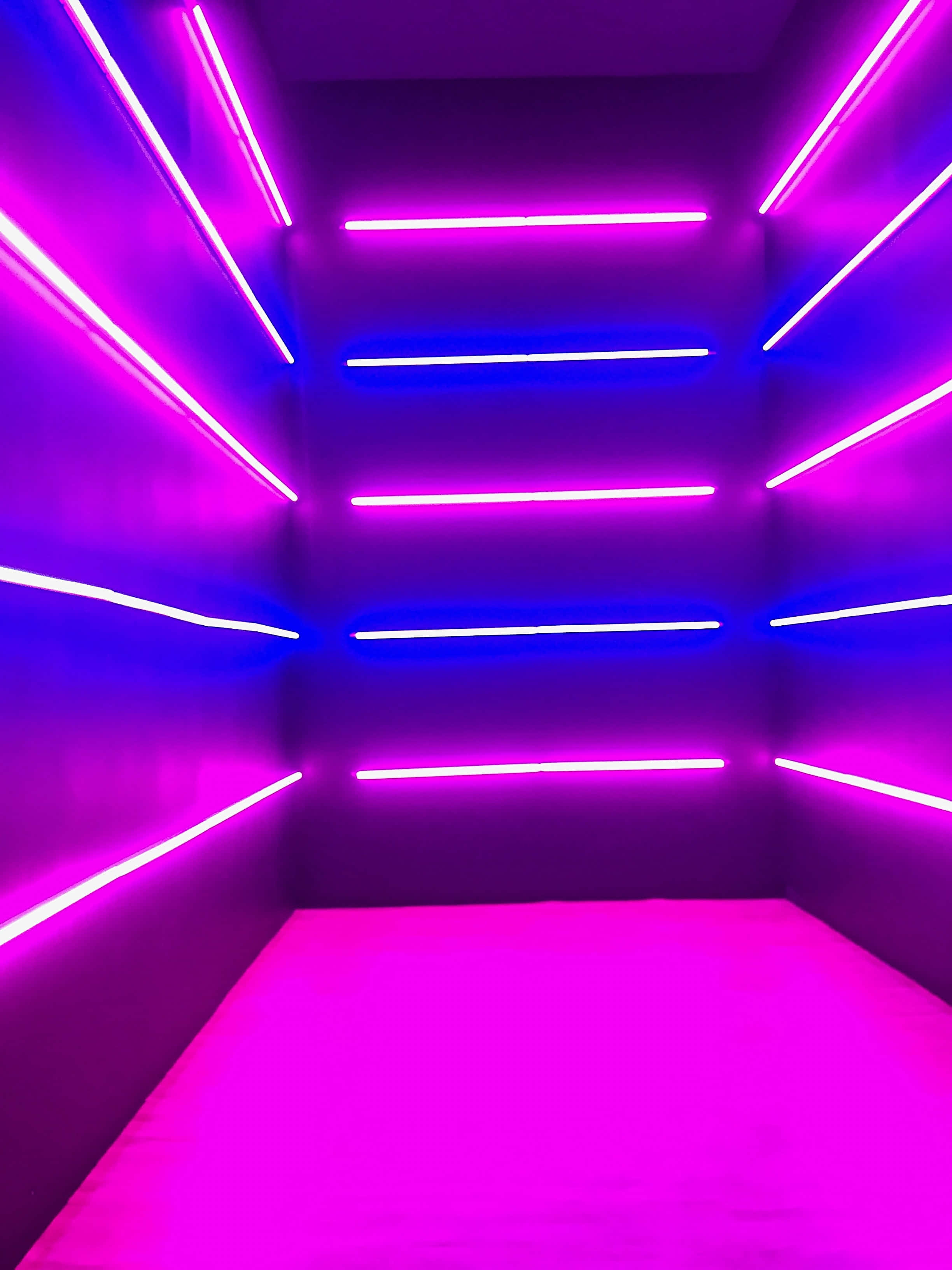 Purple Neon 桌布 壁紙 — 一個充滿未來感的房間，牆壁和天花板上佈滿了充滿活力的紫色和藍色霓虹燈。