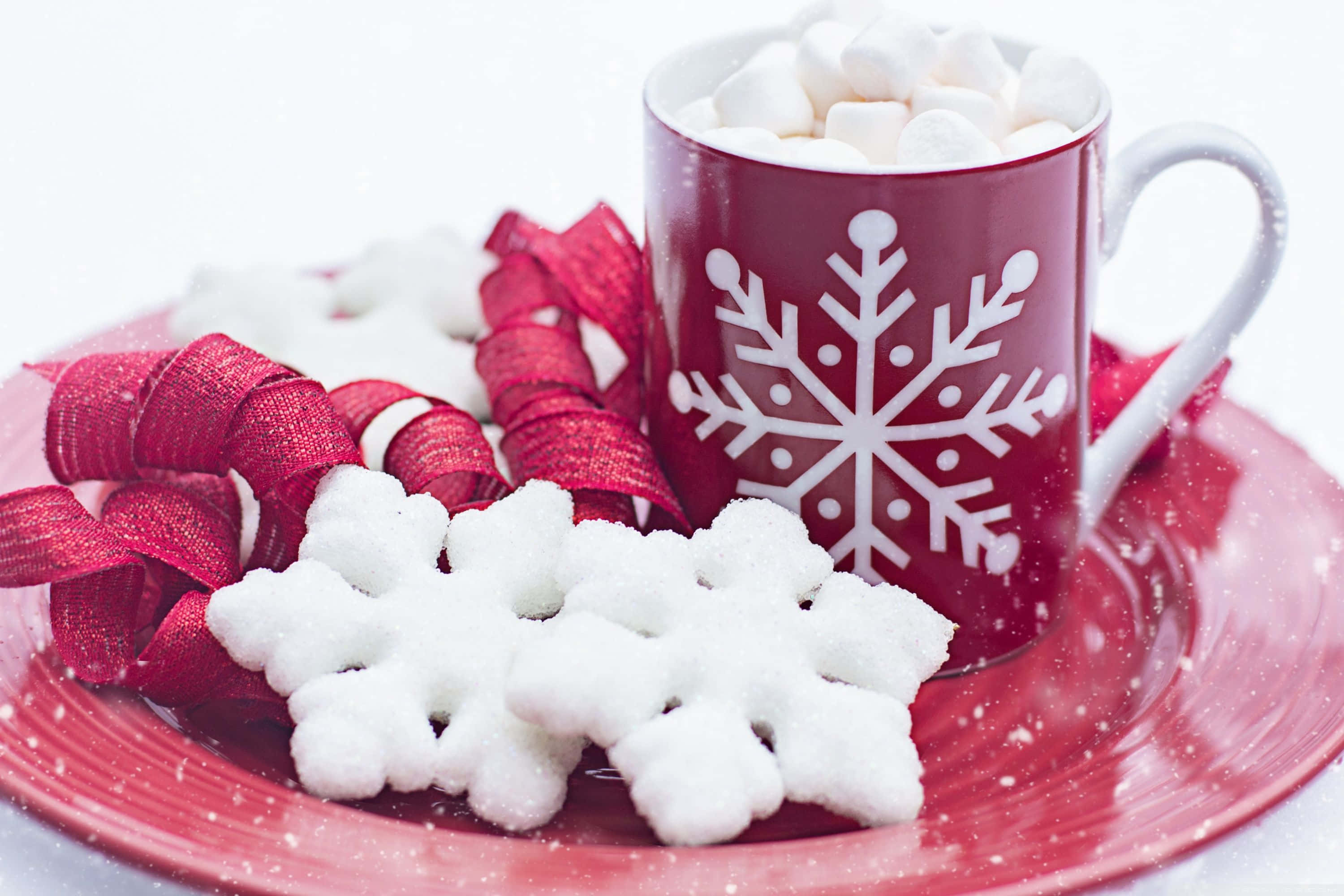 Winter Desserts 桌布 壁紙 — 一個充滿棉花糖的節日紅色馬克杯，旁邊放著一個糖雪花餅乾和紅色絲帶，放在相配的盤子上。