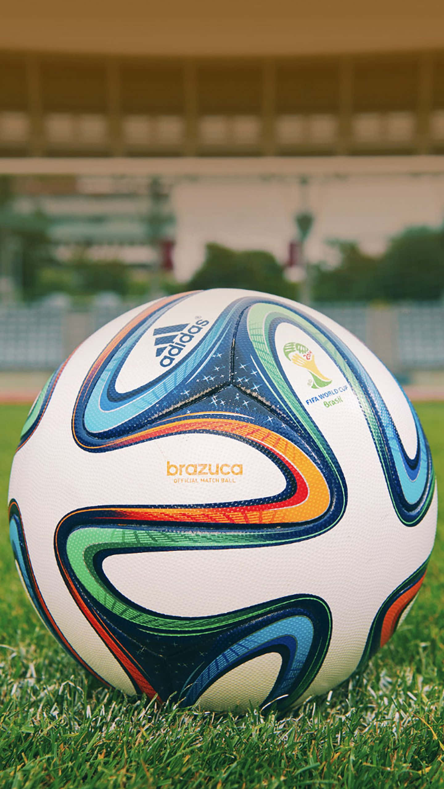 足球 桌布 壁紙 — 一個充滿活力的 Brazuca 足球放在茂盛的綠草上，背景是模糊的體育場。
