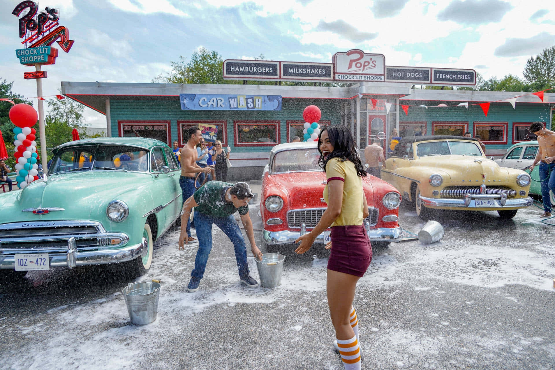 Riverdale 桌布 壁紙 — 一個充滿活力的1950年代洗車場景，人們在晴朗的天空下擦洗經典美國汽車。