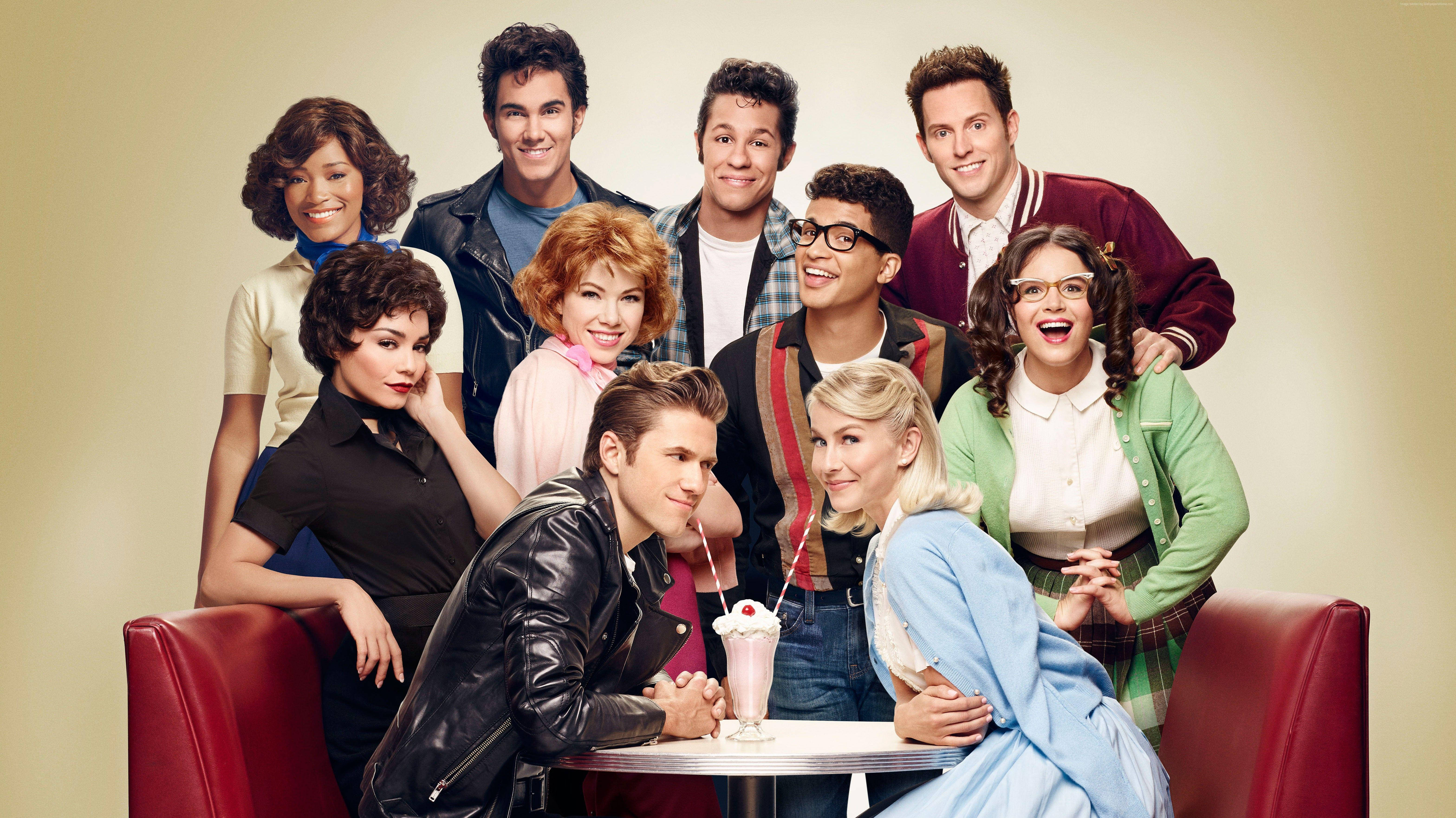 Grease 桌布 壁紙 — 一個充滿活力的1950年代餐廳場景，九位微笑的演員圍著一張放有奶昔的桌子擺姿勢。
