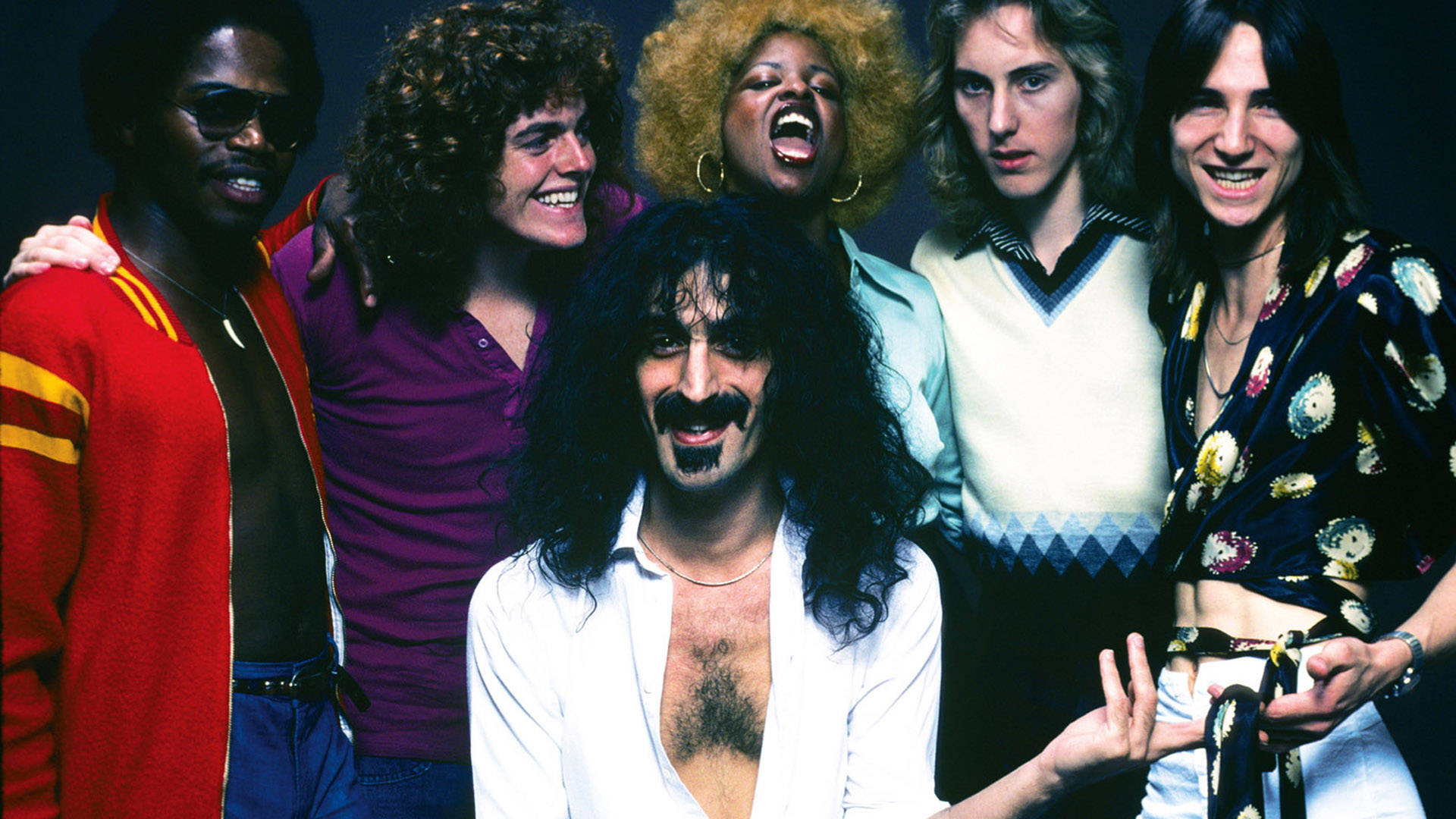 Zappa 桌布 壁紙 — 一個充滿活力的1970年代搖滾樂團在深色背景下擺出表情豐富和華麗的服裝姿勢。