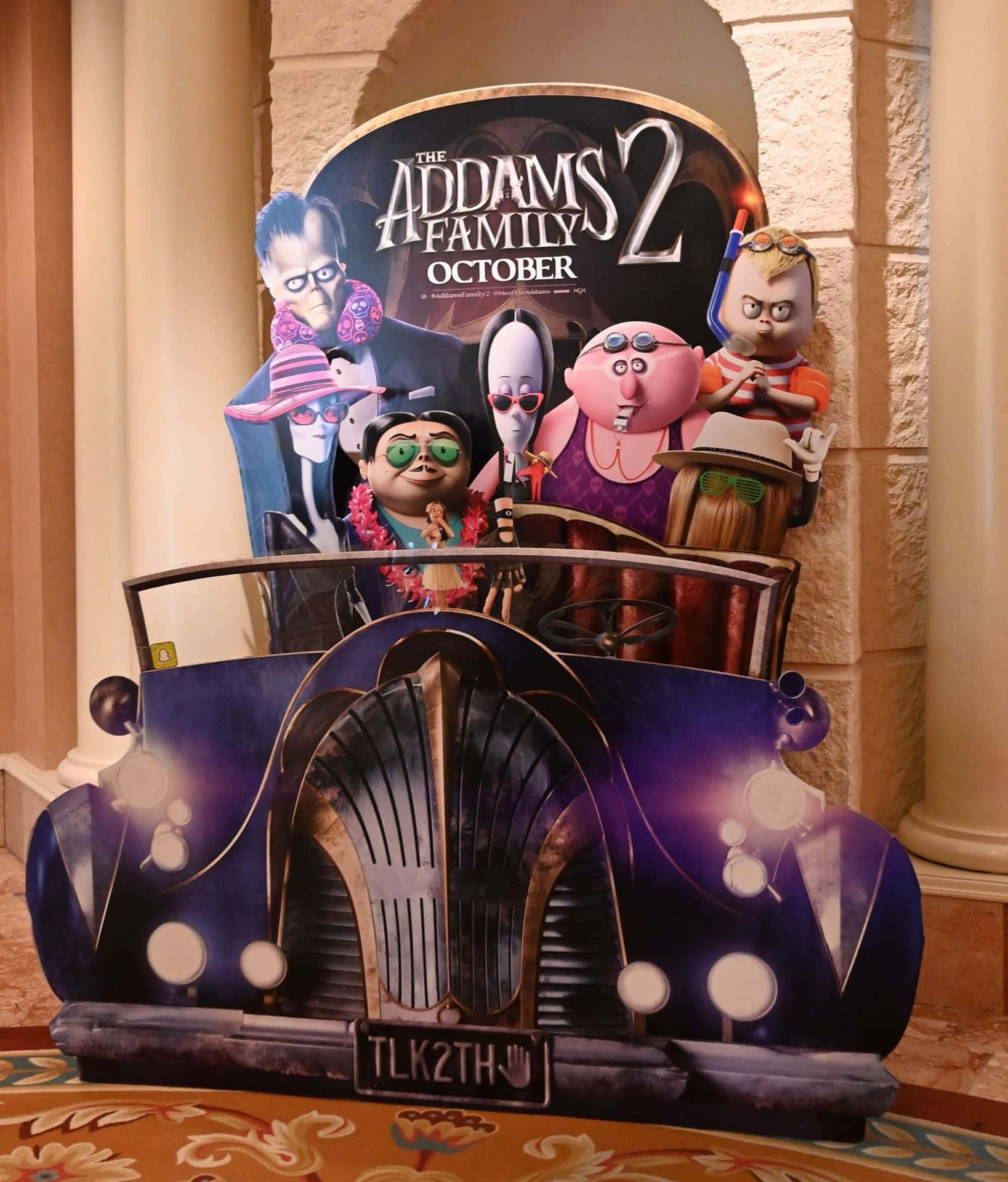 Addams Family 桌布 壁紙 — 一個充滿活力的3D宣傳剪紙，展示The Addams Family 2角色在紫色復古車中，車牌為'TLK2TH'。