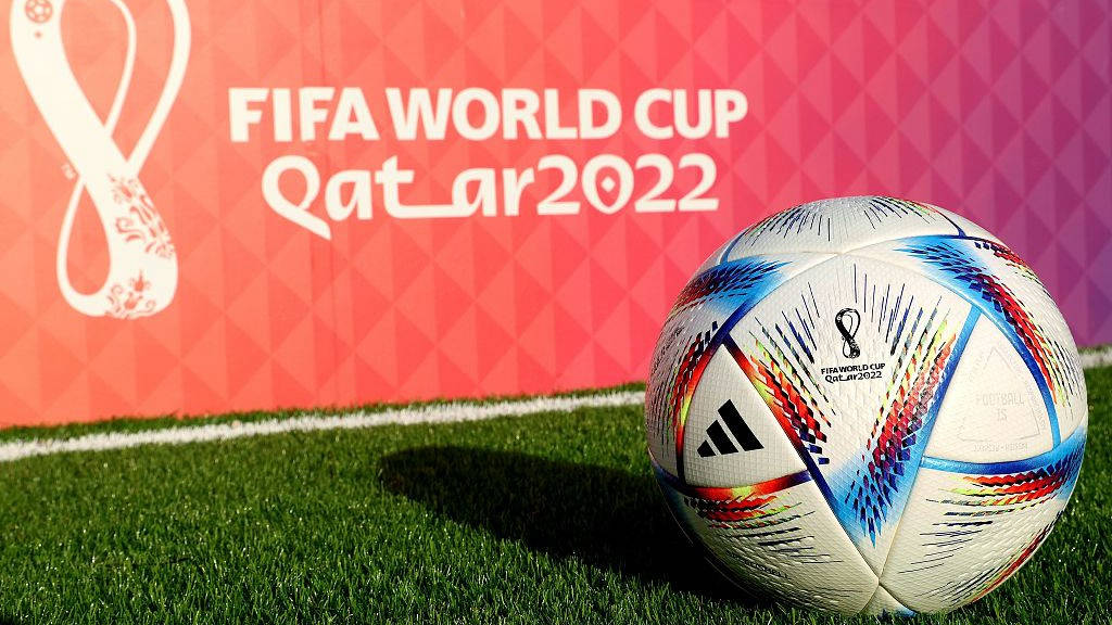 足球 桌布 壁紙 — 一個充滿活力的FIFA世界盃卡達2022足球放在綠色草地上，背景是粉紅色圖案和活動品牌標誌。