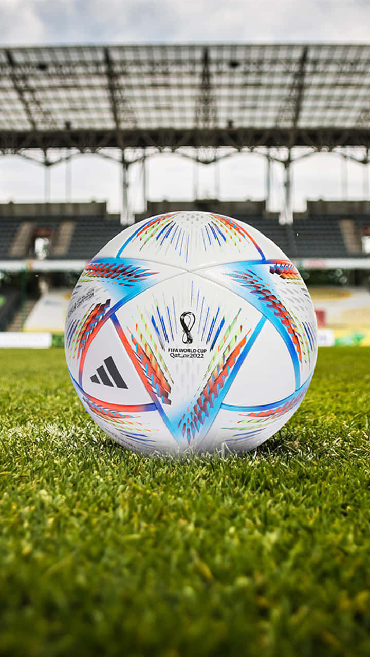 足球 桌布 壁紙 — 一個充滿活力的FIFA世界盃卡達2022足球，放在陰天下一片空蕩蕩的體育館內茂密的綠草上。