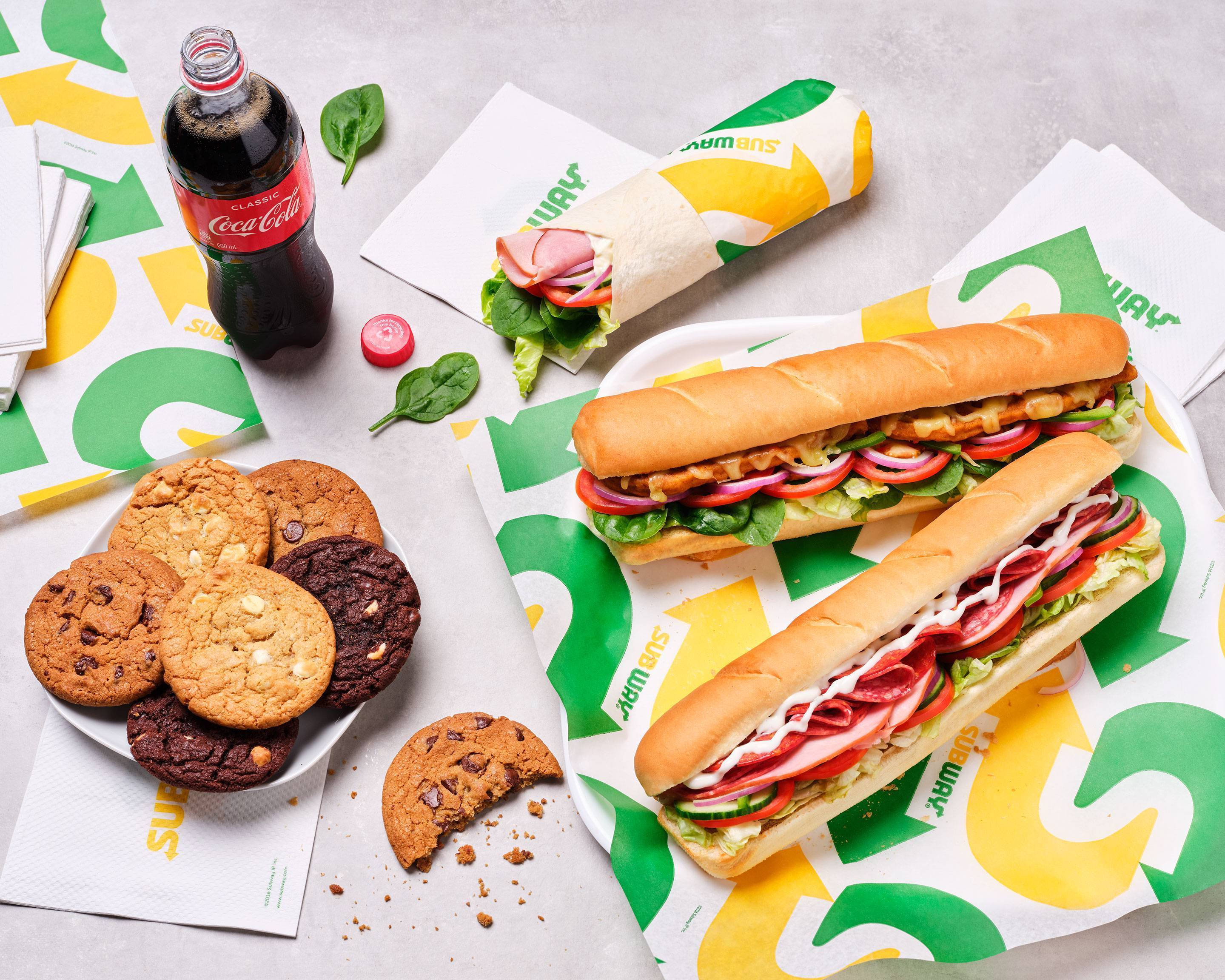 三明治 桌布 壁紙 — 一個充滿活力的Subway餐點，包括新鮮三明治、餅乾和一瓶可口可樂，放在品牌紙上。