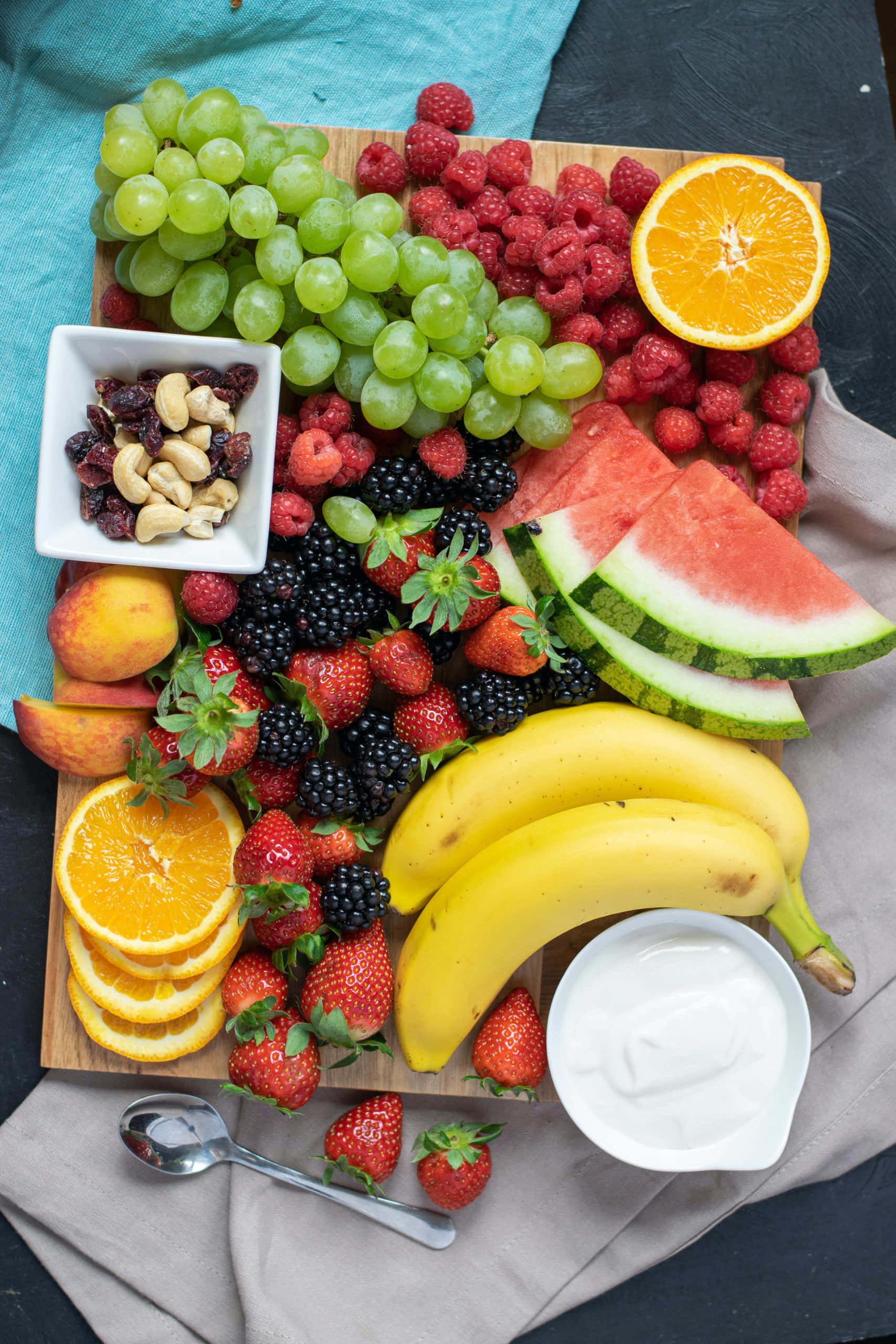 Fruit 桌布 壁紙 — 一個充滿活力的俯拍鏡頭，展示一塊木板上擺放著各種新鮮水果和堅果，並置於有紋理的布料上。