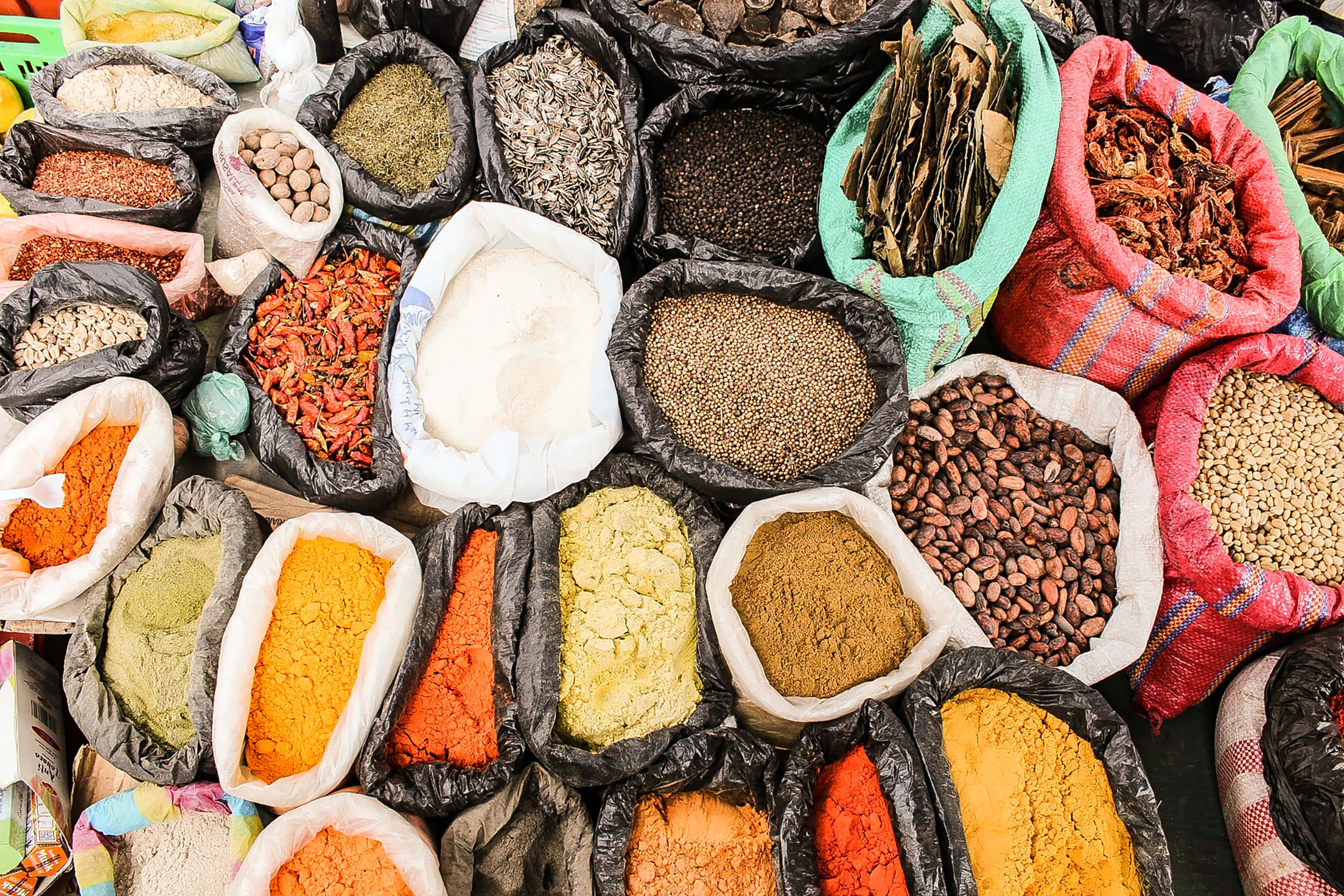 Spices 桌布 壁紙 — 一個充滿活力的俯瞰視角，展示繁忙市場攤位上色彩繽紛的香料和穀物袋。