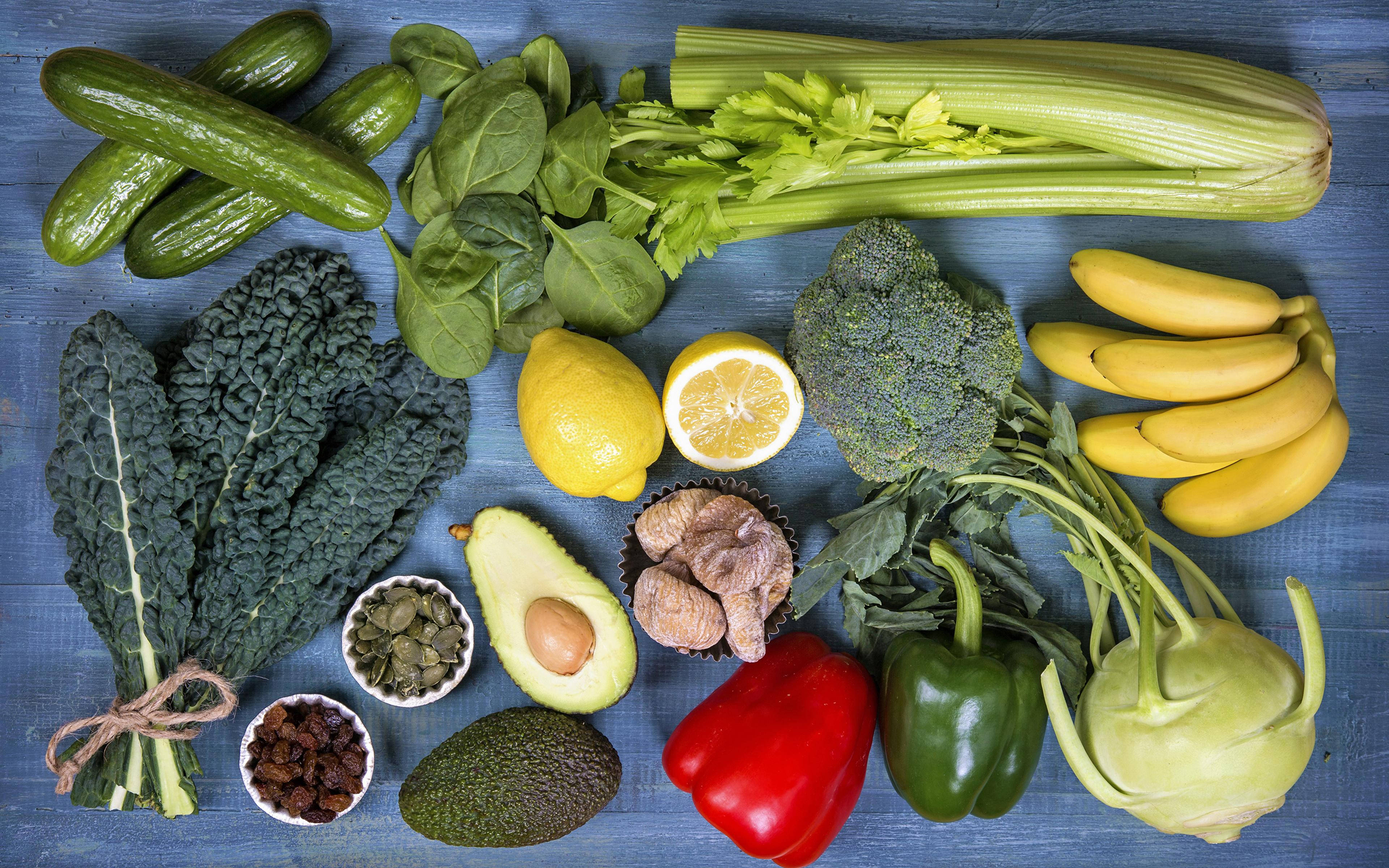 Avocado 桌布 壁紙 — 一個充滿活力的俯視排列，包括小黃瓜、檸檬、香蕉和青花菜在帶有紋理的藍色表面上。