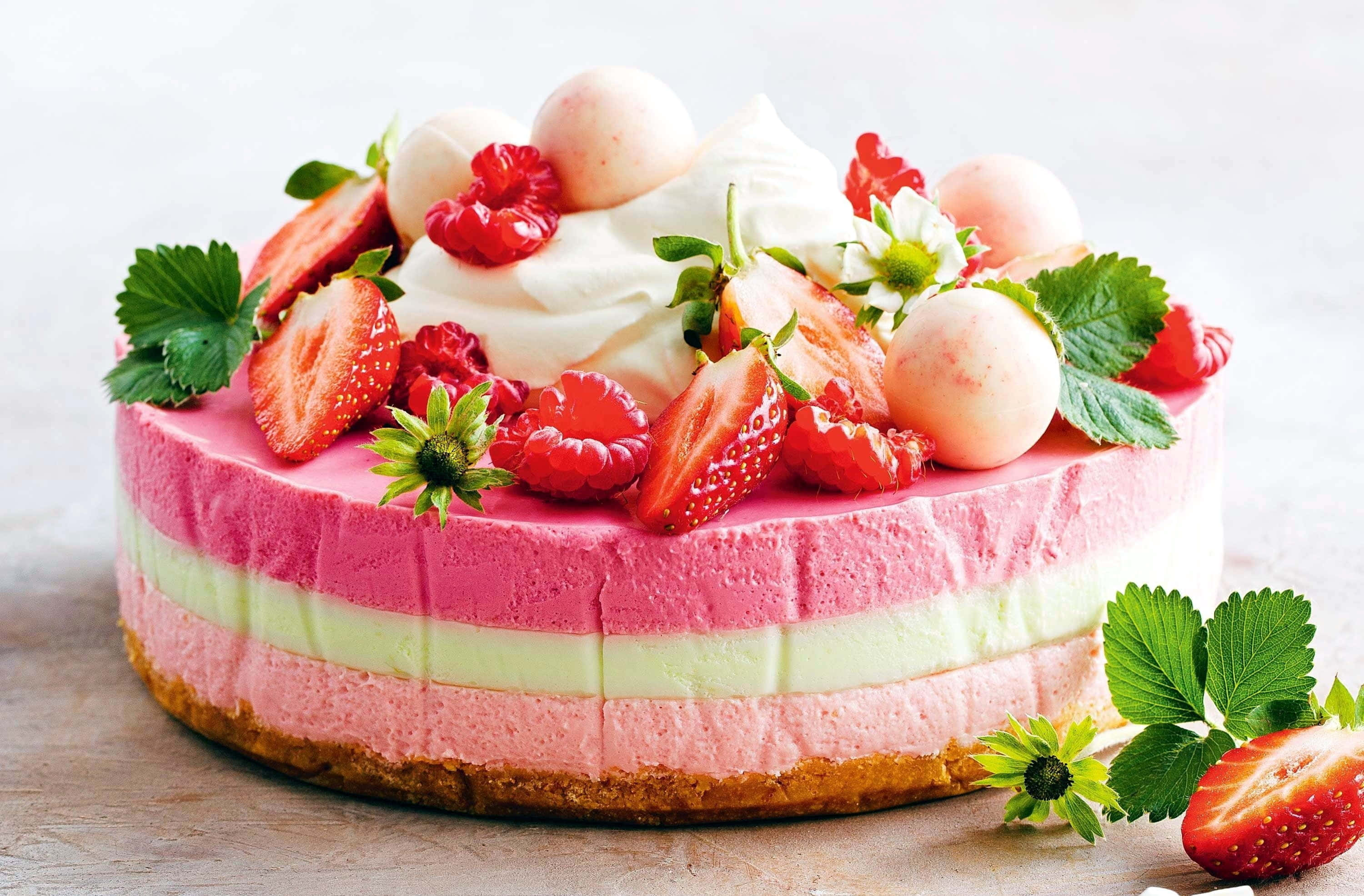 Spring Desserts 桌布 壁紙 — 一個充滿活力的分層草莓起司蛋糕，上面鋪滿新鮮莓果、鮮奶油和綠葉，放在木質表面上。