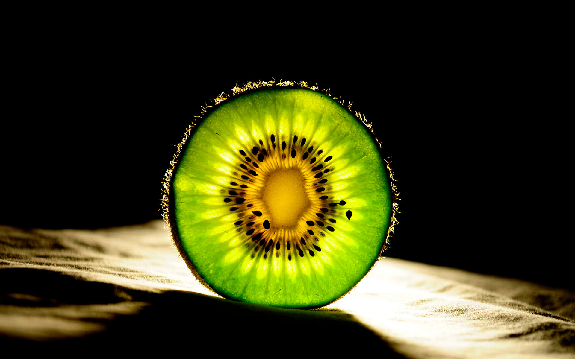 Kiwi 桌布 壁紙 — 一個充滿活力的切片奇異果在黑色背景下戲劇性的聚光燈下發光。