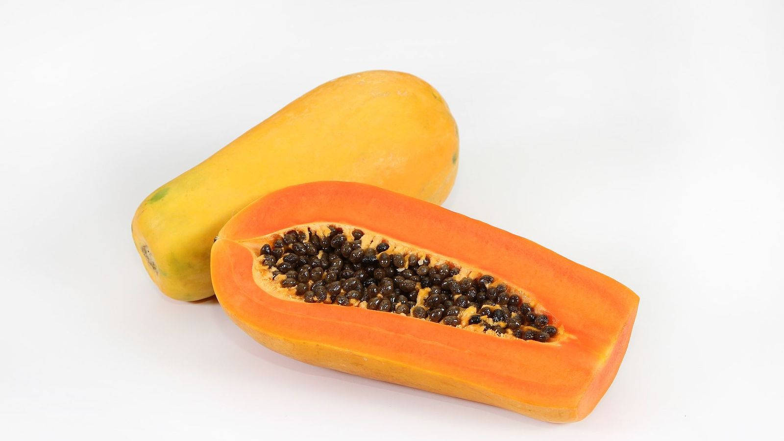Fruit 桌布 壁紙 — 一個充滿活力的半切木瓜，帶有多汁的橙色果肉和黑色種子，放在一個完整的黃色木瓜旁邊，背景是乾淨的白色。