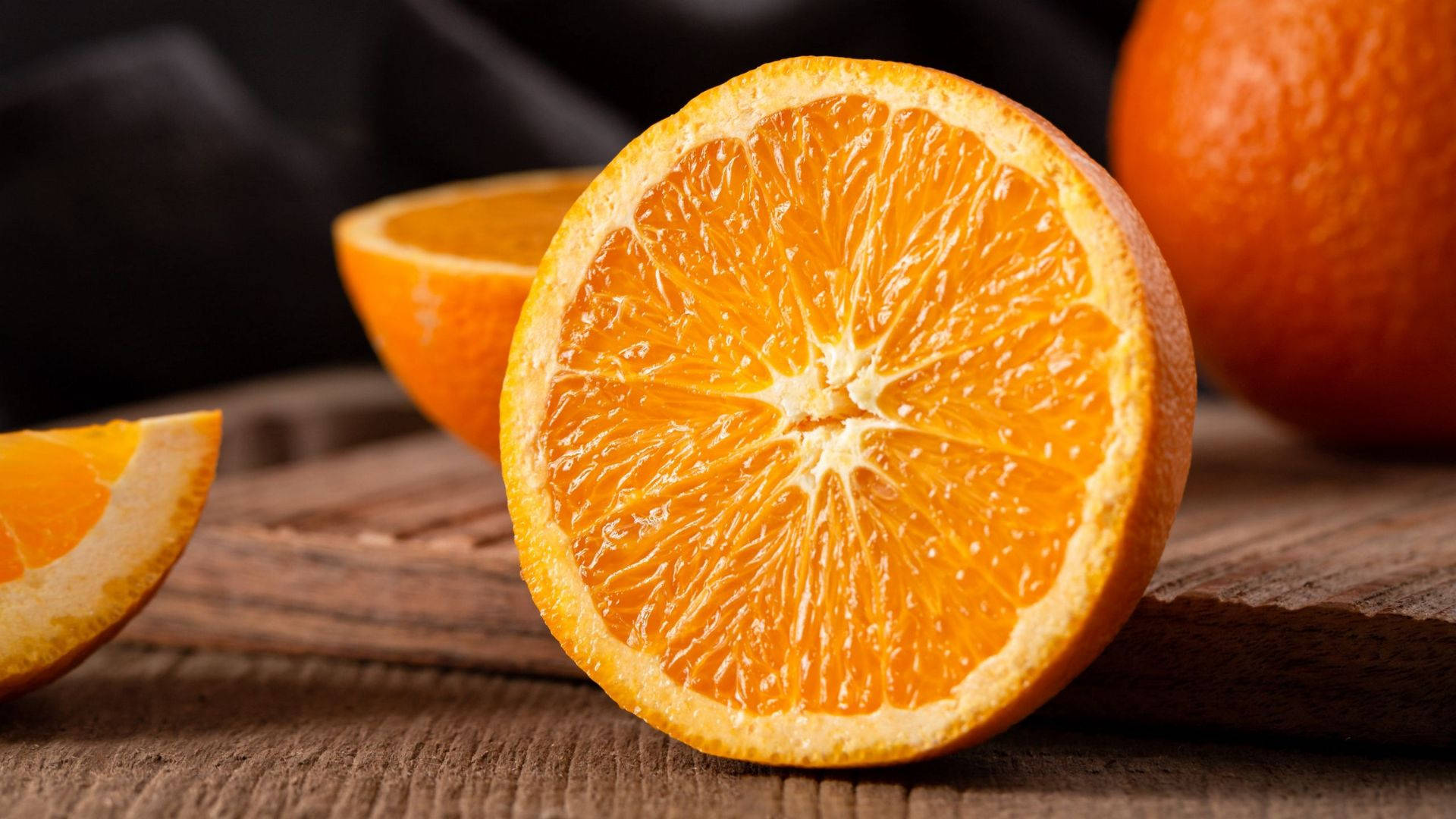 Orange Fruit 桌布 壁紙 — 一個充滿活力的半切橙子在深色背景的鄉村木質表面上展現出多汁的果瓣。