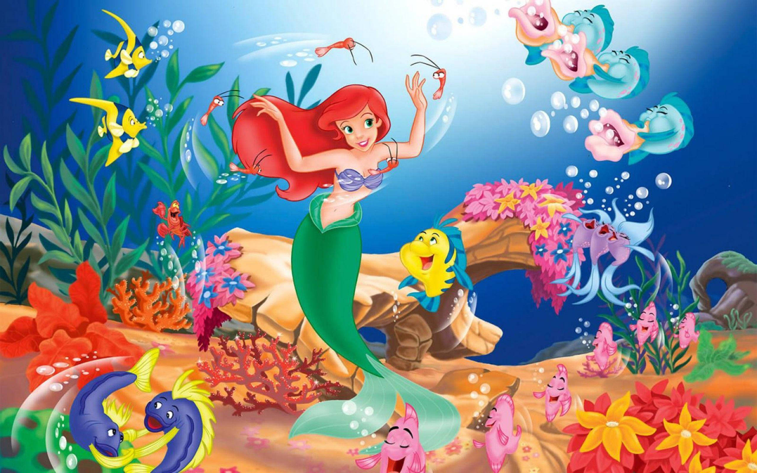愛麗兒 桌布 壁紙 — 一個充滿活力的卡通美人魚，紅髮綠尾，在陽光明媚的海底王國中，在色彩繽紛的珊瑚和微笑的海洋生物之間快樂地跳舞。