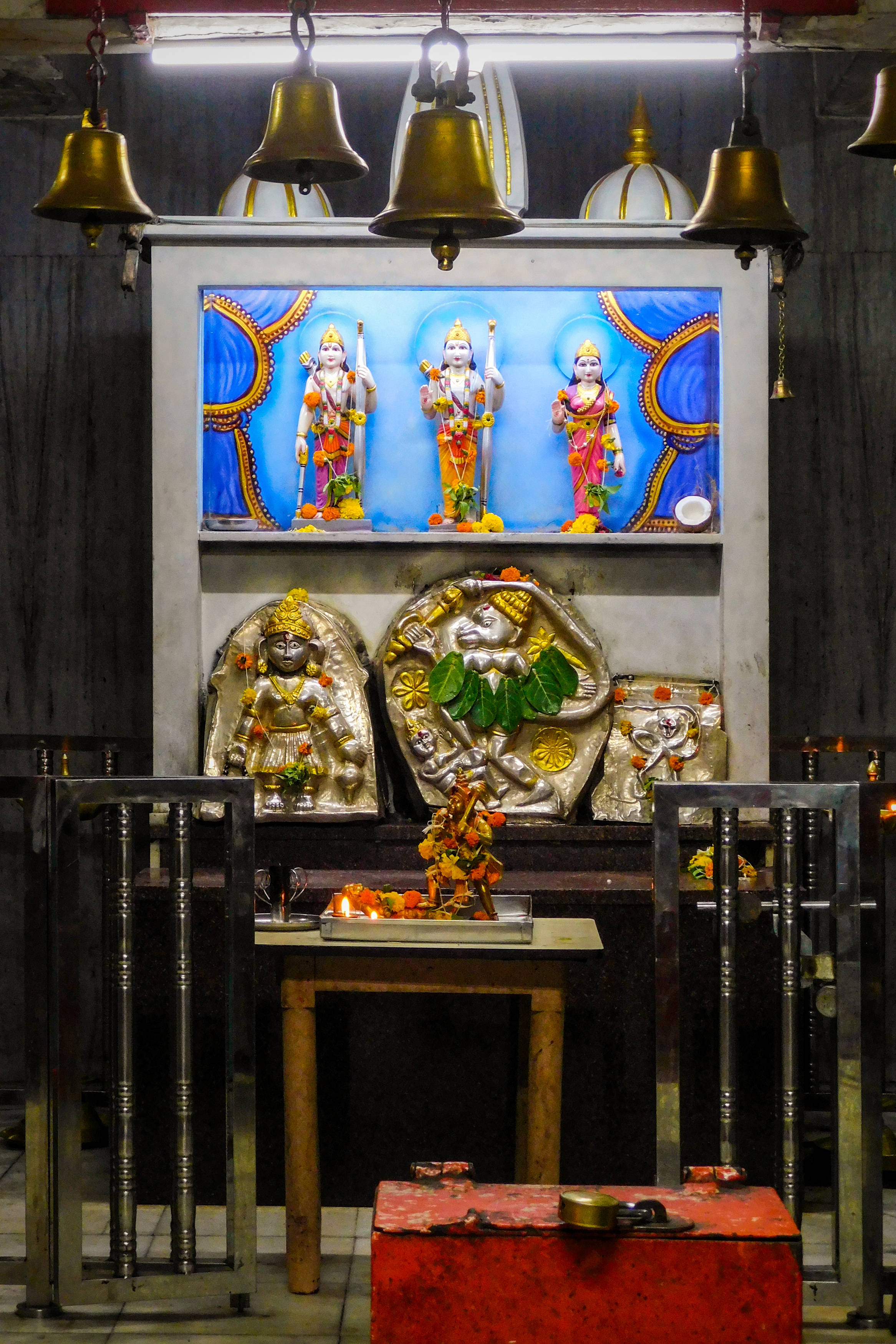 Hindu Temple 桌布 壁紙 — 一個充滿活力的印度教聖殿，金色鈴鐺懸掛在色彩繽紛的神像和銀色偶像上方，在溫暖的人造燈光下。