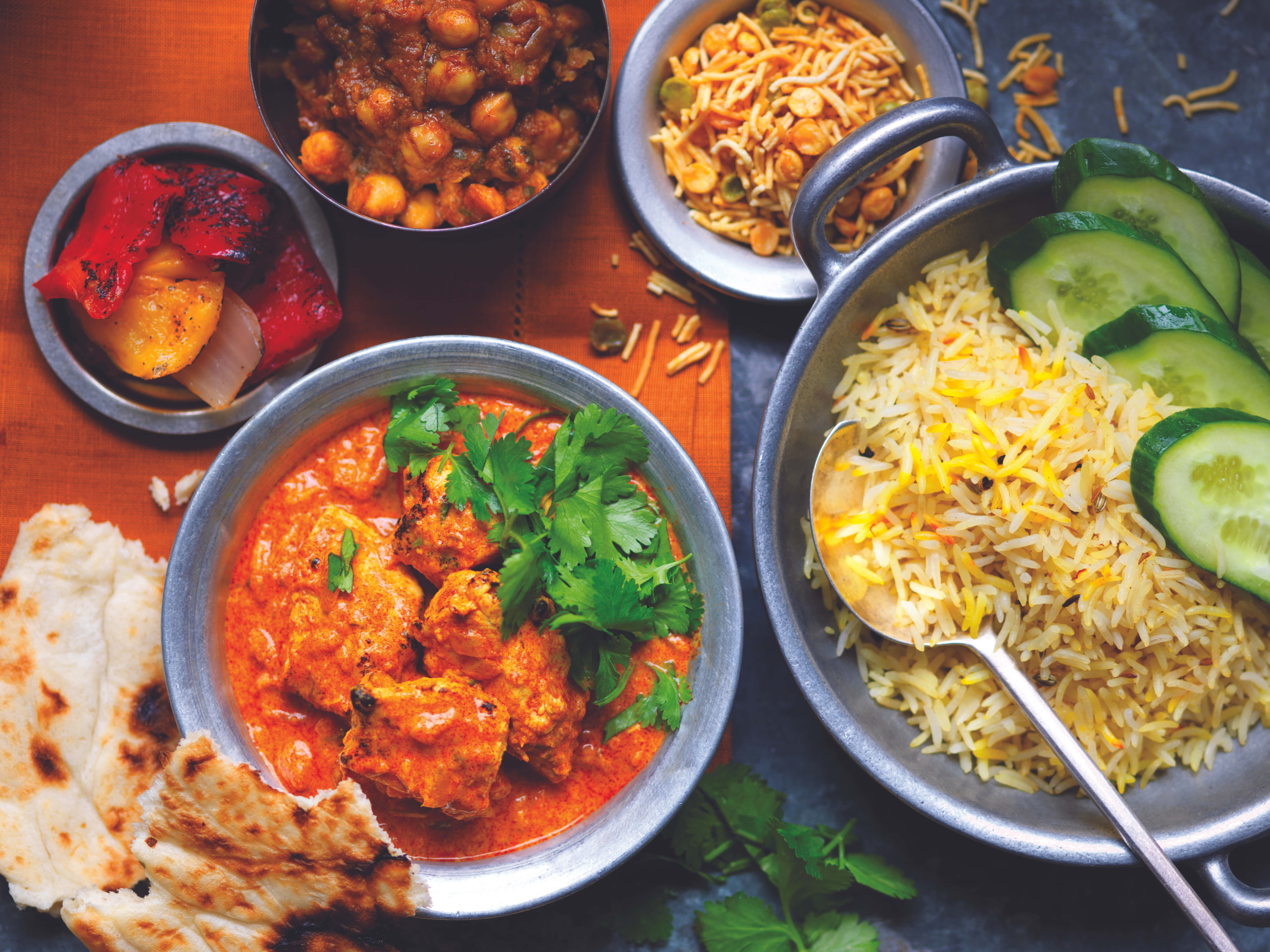 Indian 桌布 壁紙 — 一個充滿活力的印度菜餚拼盤，包括咖哩雞、米飯、印度烤餅和鷹嘴豆咖哩，盛放在木桌上的金屬碗中。