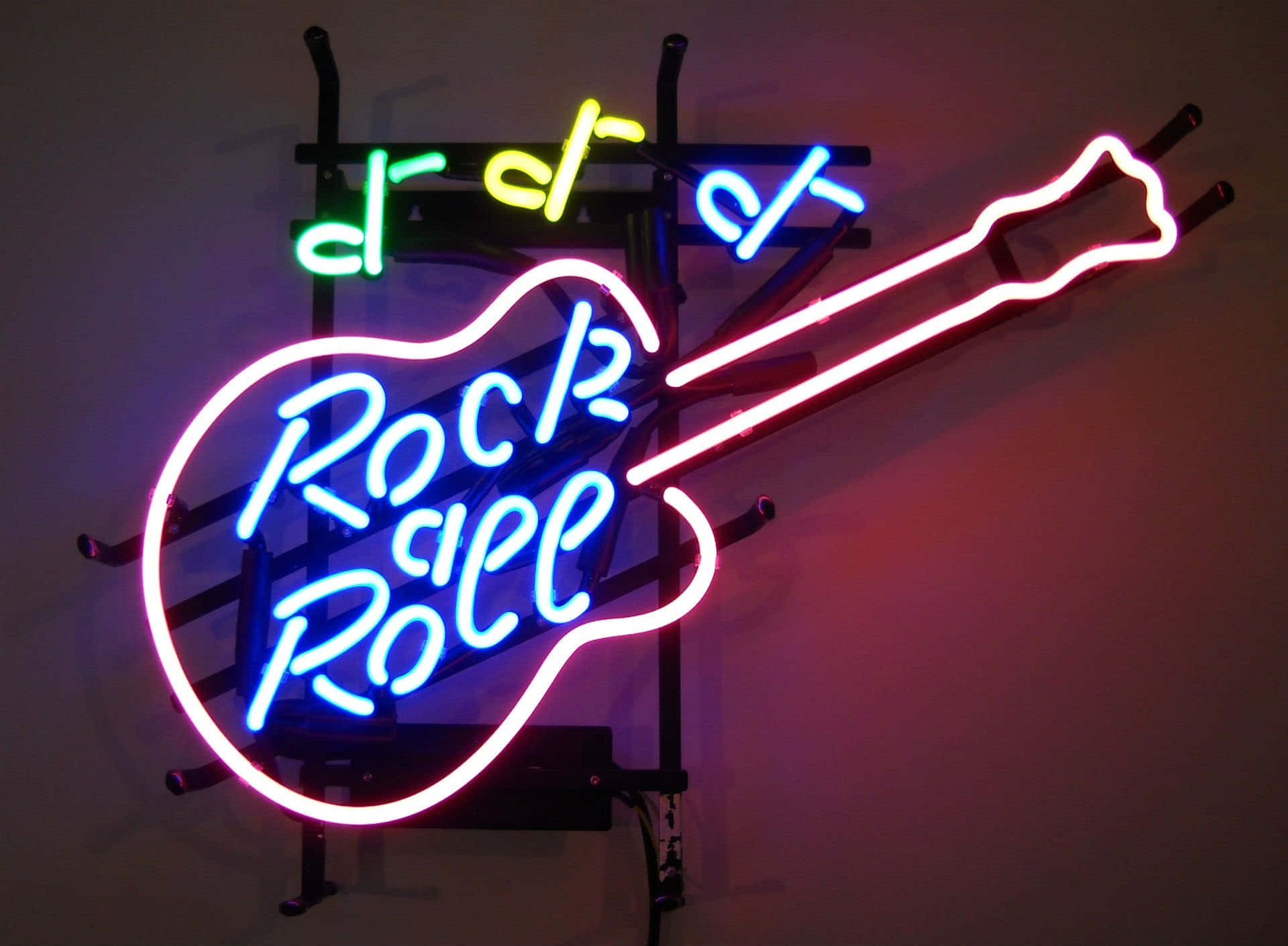 neon sign 桌布 壁紙 — 一個充滿活力的吉他形霓虹燈牌，上面有藍色字母 'Rock Roll' 和彩色音符，在黑暗的牆壁上發光。