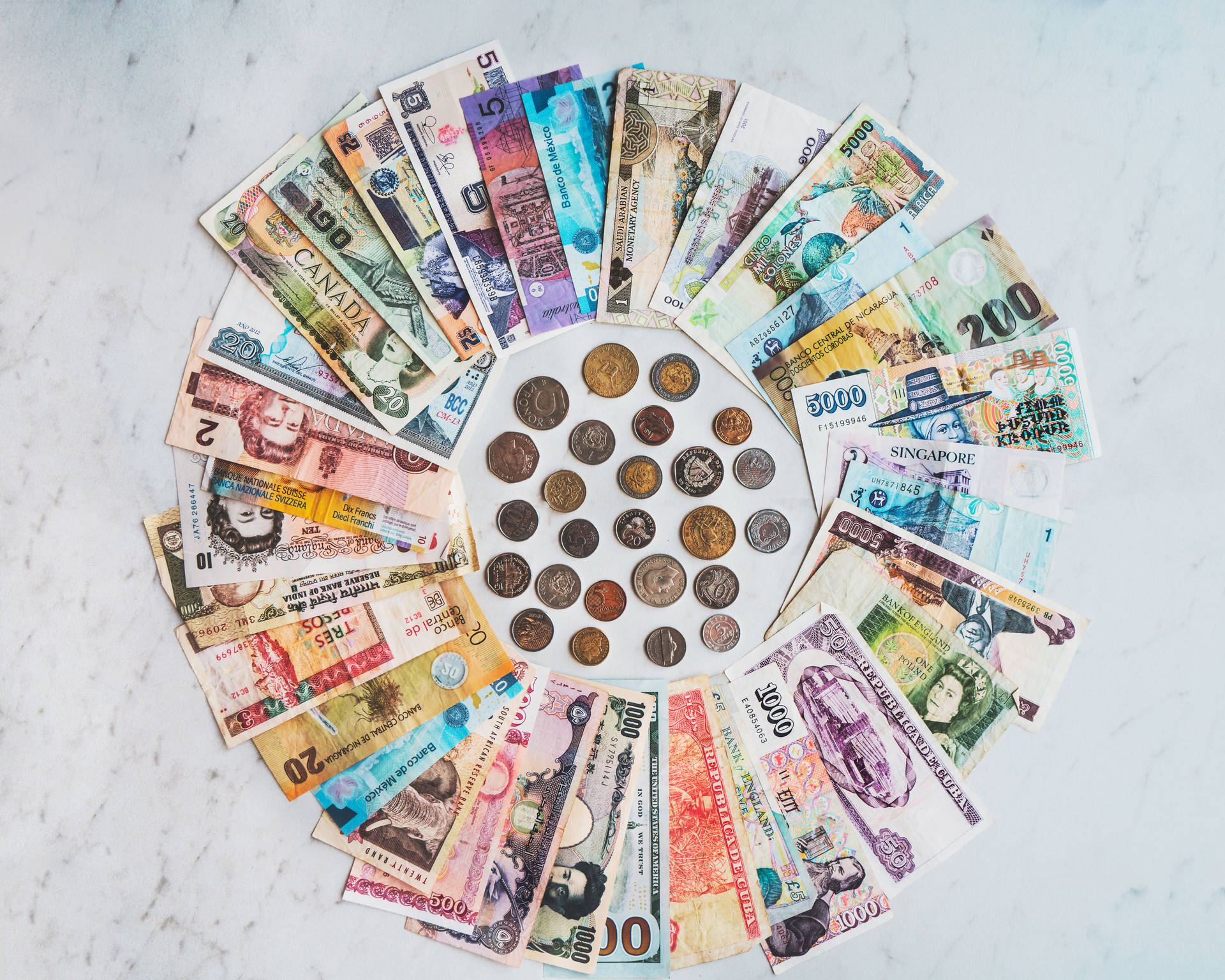 Money 桌布 壁紙 — 一個充滿活力的圓形排列，全球各國的紙幣和硬幣從大理石表面放射而出，展示國際貨幣的多樣性。