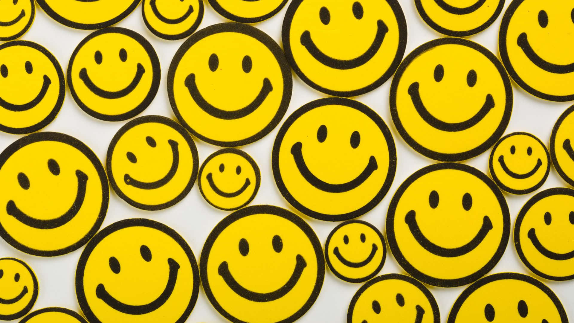 Smiley 桌布 壁紙 — 一個充滿活力的圖案，黃色笑臉貼紙帶有黑色輪廓，散落在白色背景上。