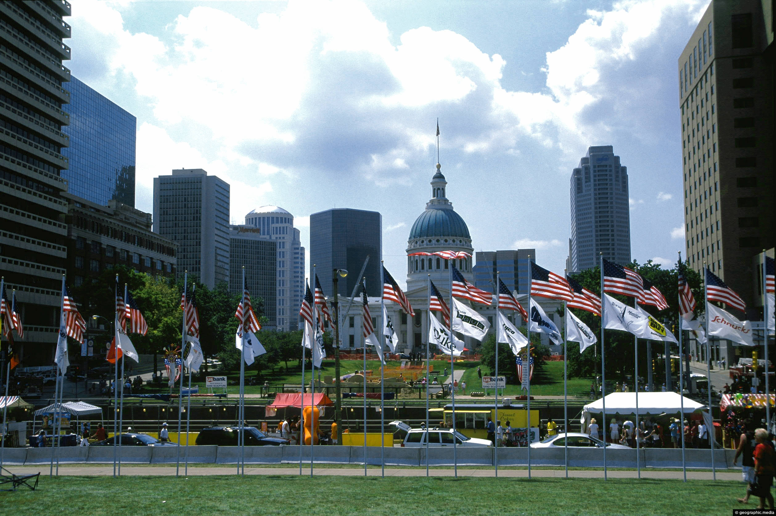 USA Flag 桌布 壁紙 — 一個充滿活力的城市景觀，圓頂國會大廈被美國國旗和現代摩天大樓環繞，天空部分多雲。