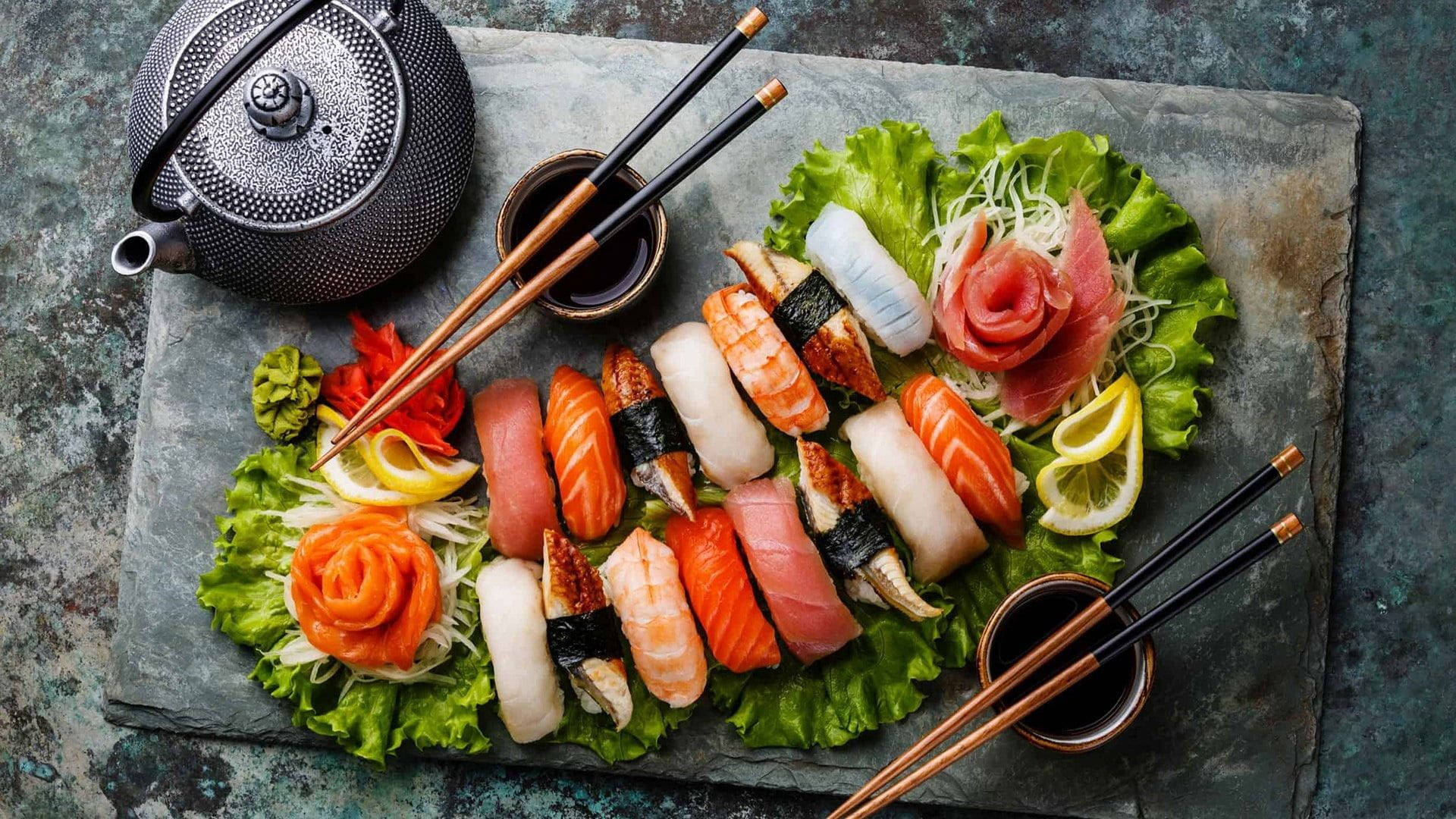 Sushi 桌布 壁紙 — 一個充滿活力的壽司拼盤，上面有各種卷物和刺身，藝術地排列在生菜上，配以芥末、生薑和醬油。