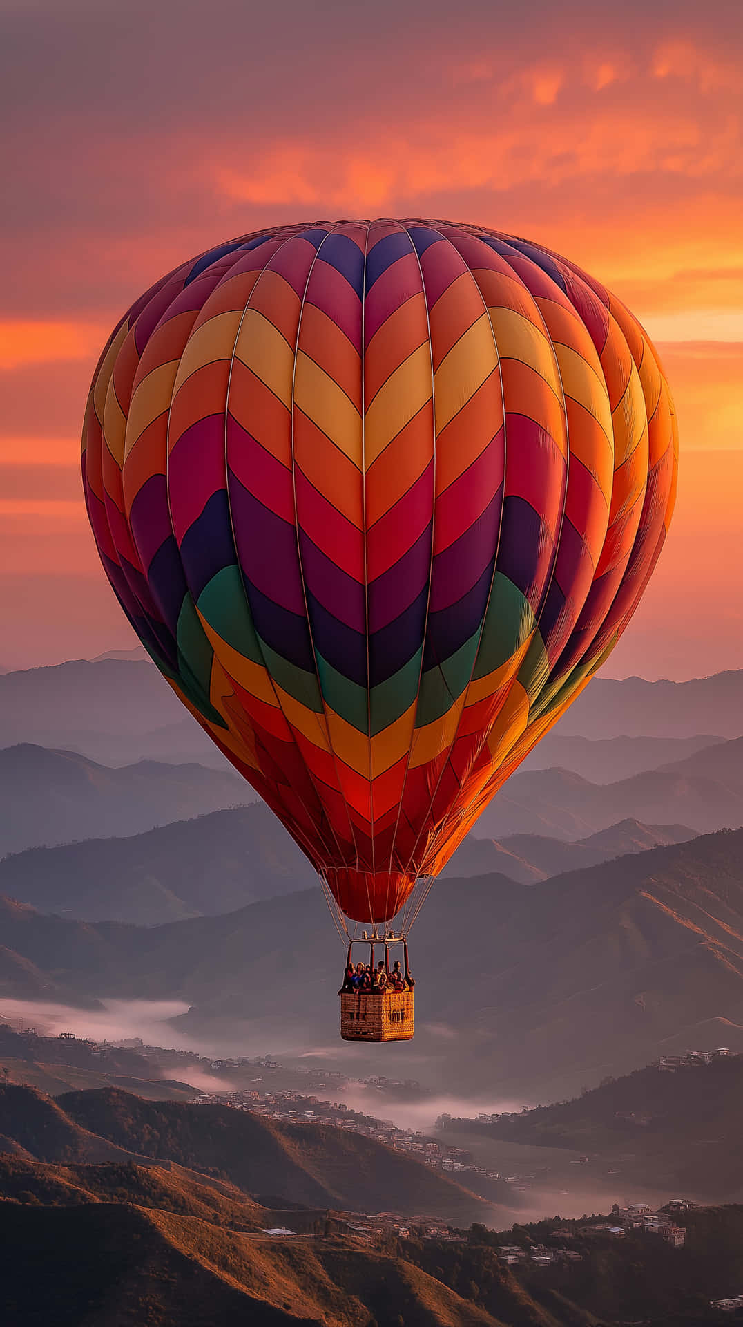 Mountain Balloon Ride 壁紙 — 一個充滿活力的多色熱氣球漂浮在日落時分霧氣繚繞的山脈之上，天空呈現橙色、粉紅色和紫色。