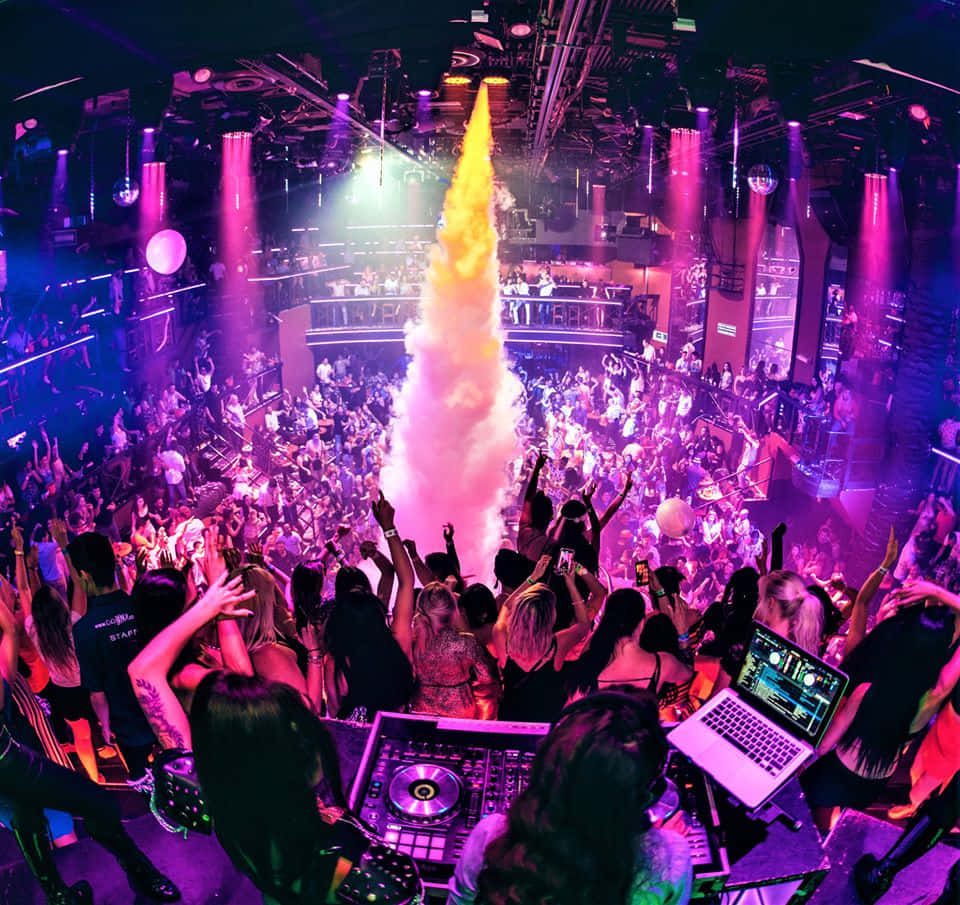 Party 桌布 壁紙 — 一個充滿活力的夜店場景，人群在紫色燈光下跳舞，金色煙霧柱從舞台噴出。