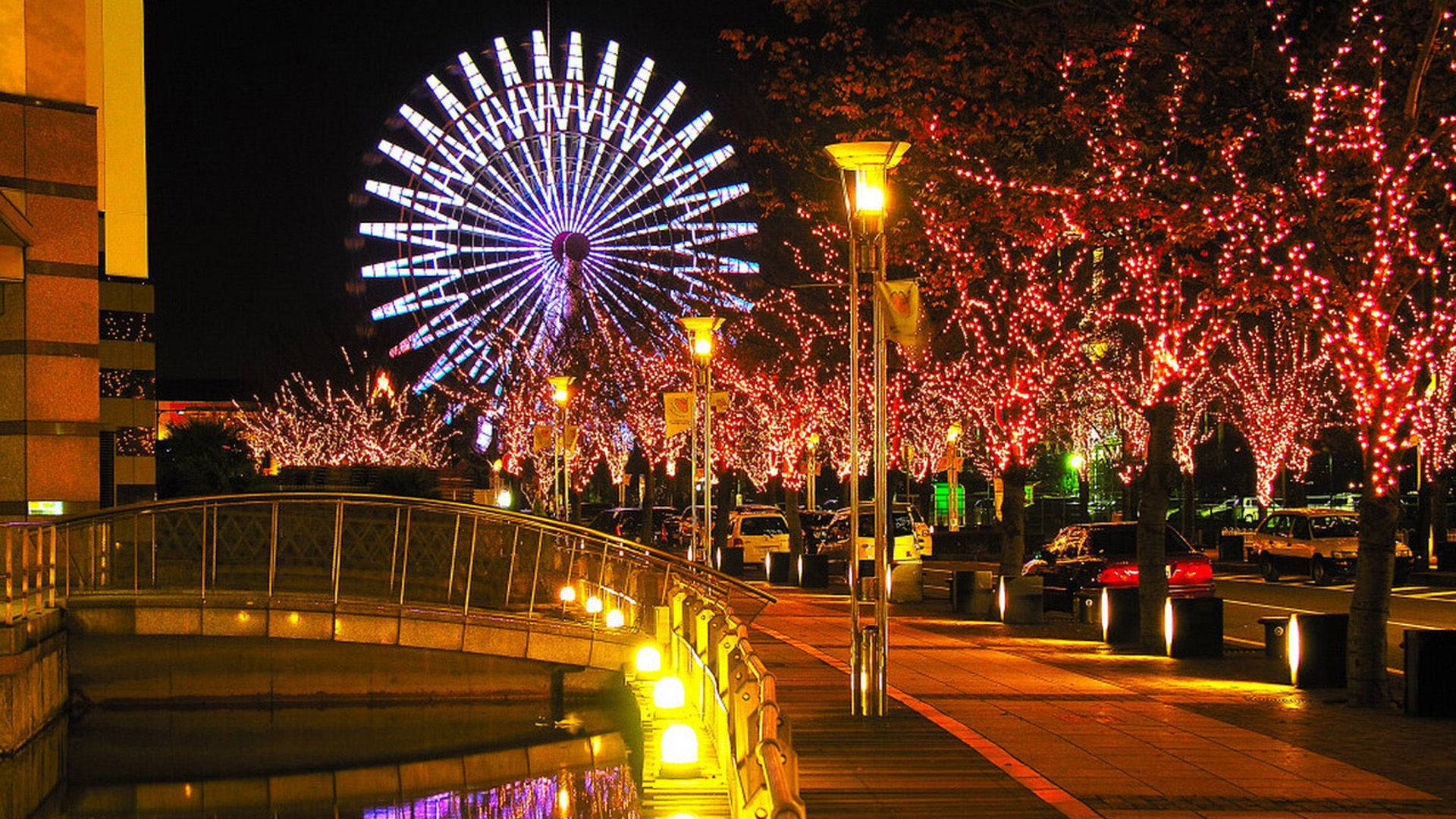 橘色城市 桌布 壁紙 — 一個充滿活力的夜景，特色是發光的摩天輪和沿著行人天橋被紅燈包裹的樹木。