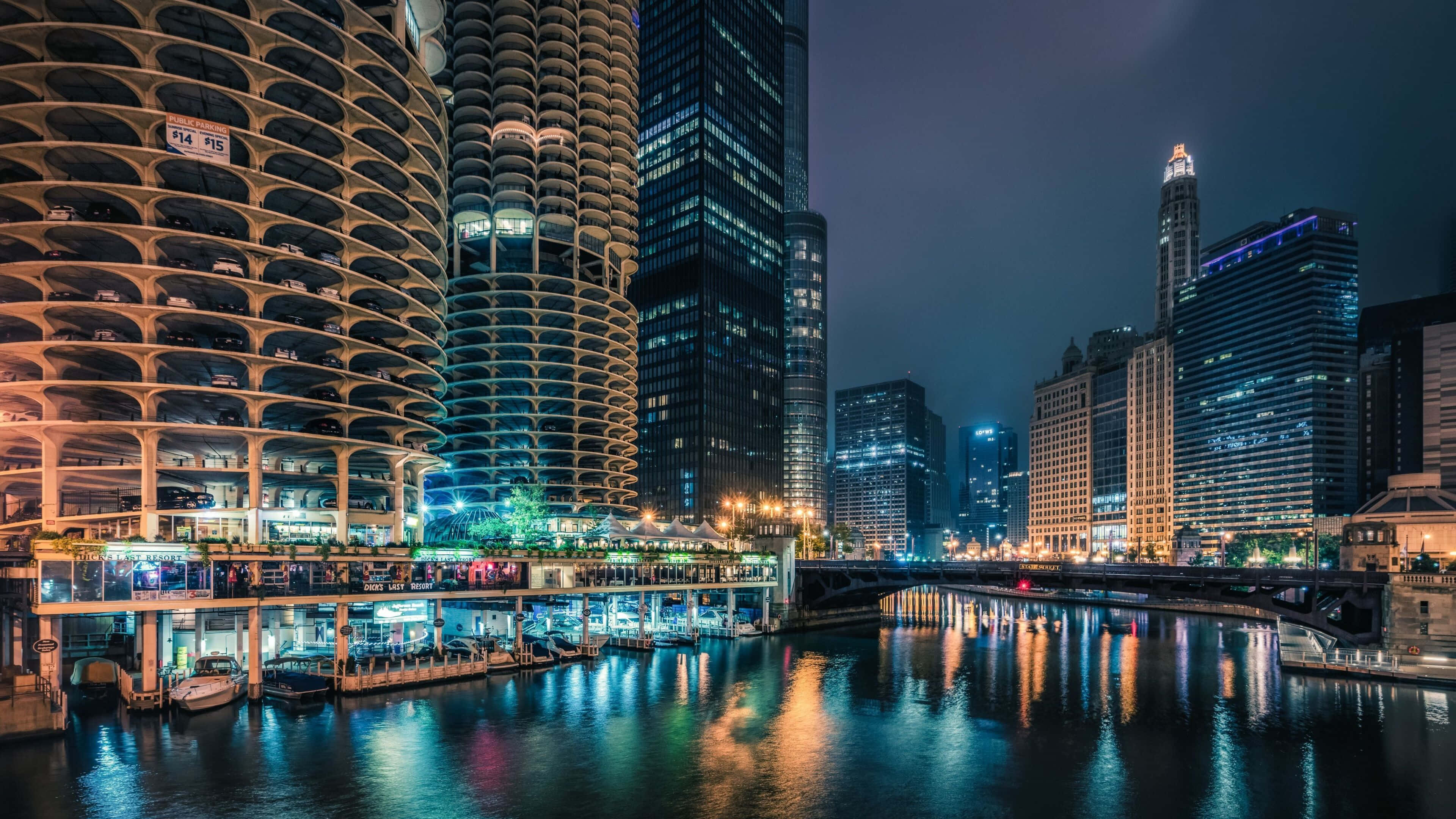 高清 桌布 壁紙 — 一個充滿活力的夜景城市景觀，在黑暗的天空下，燈火通明的摩天大樓倒映在平靜的河流中。