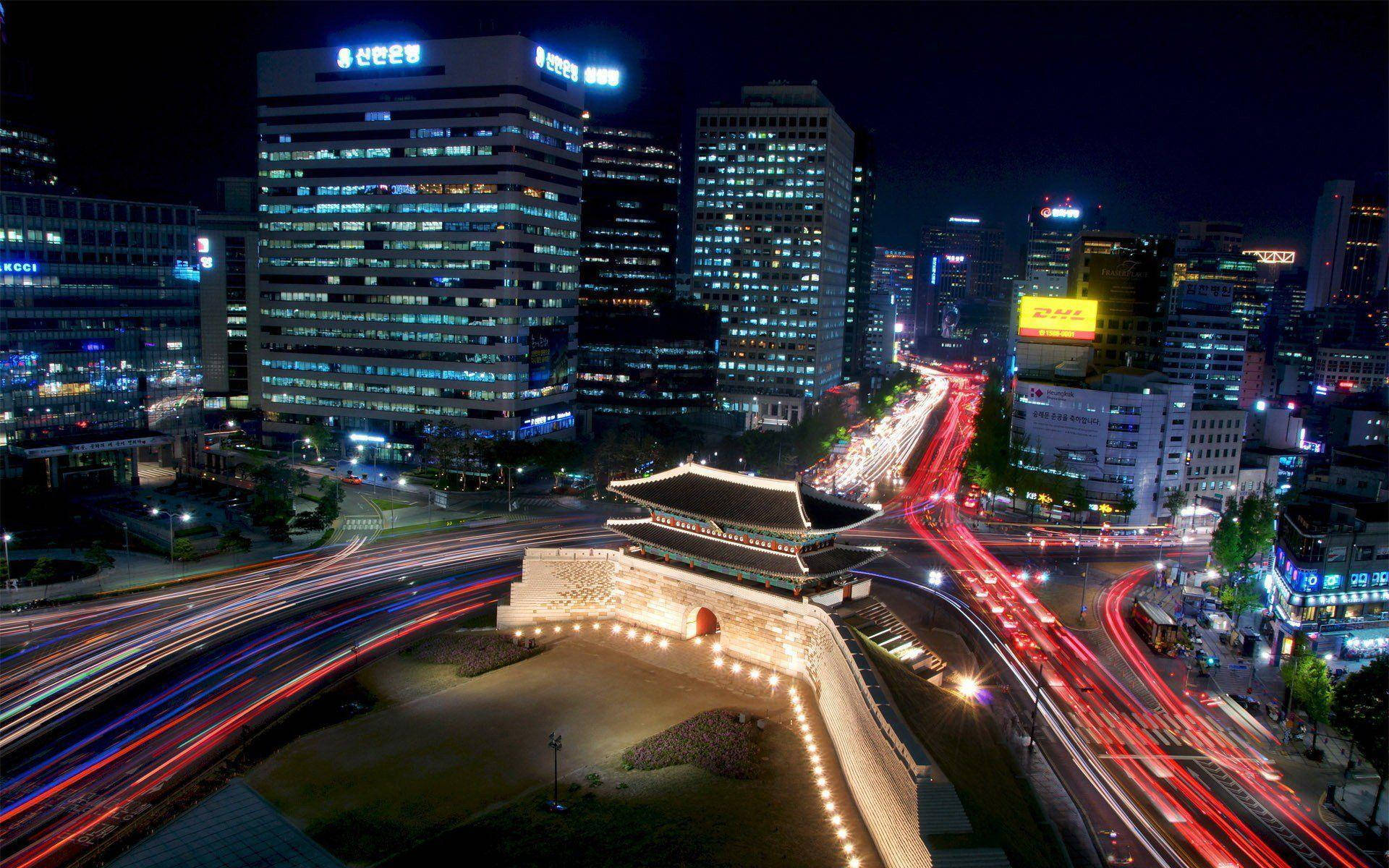 南韓 桌布 壁紙 — 一個充滿活力的夜景城市景觀，發光的摩天大樓和流動的交通環繞著一座歷史悠久的照明大門。