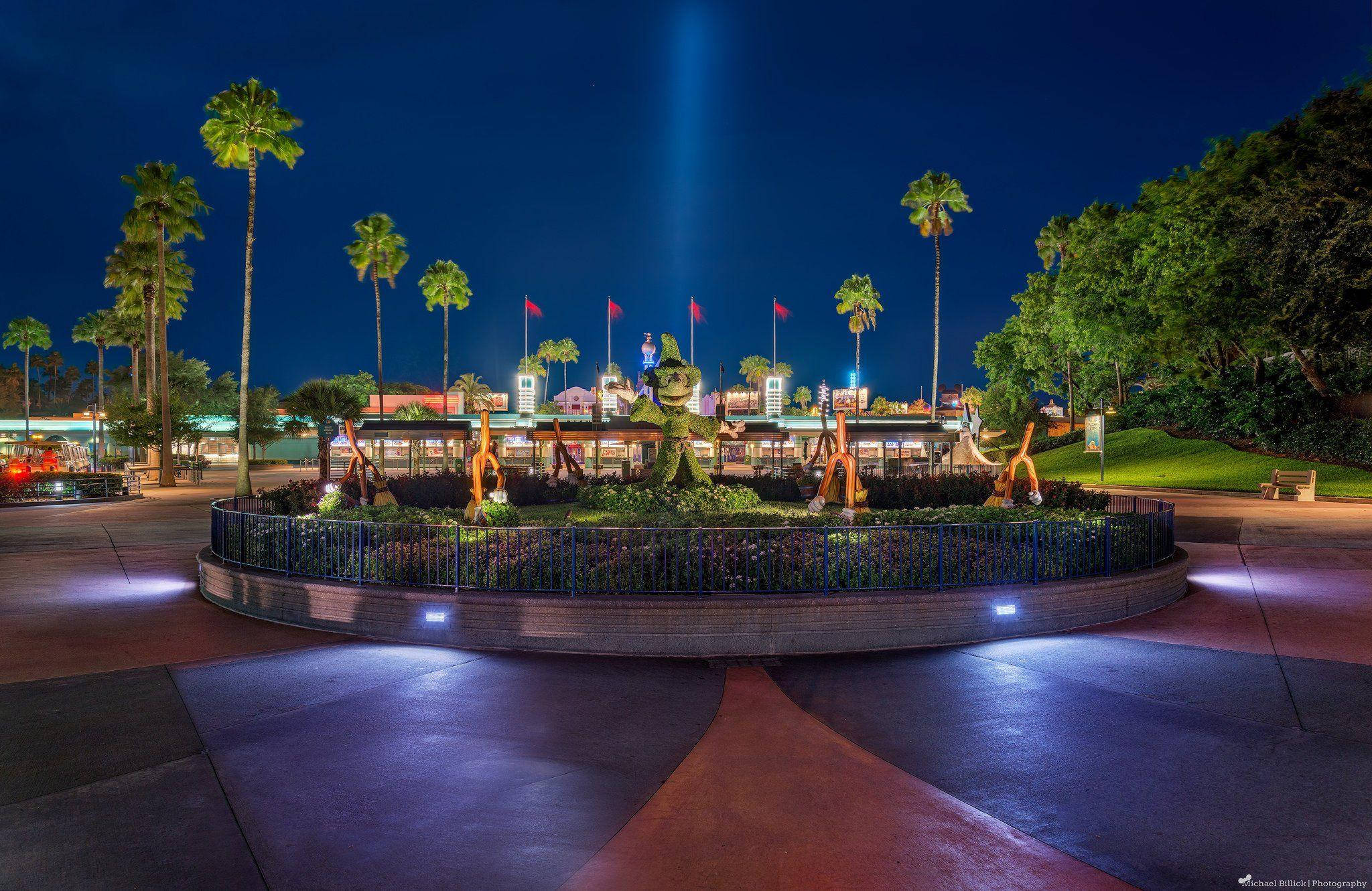 Universal Studios 桌布 壁紙 — 一個充滿活力的夜間主題公園場景，被五彩繽紛的燈光照亮，周圍環繞著棕櫚樹。
