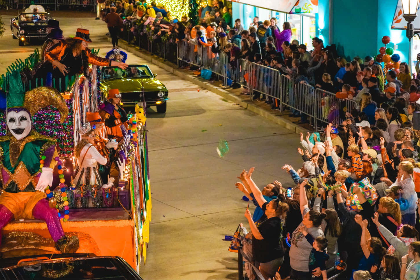 Mardi Gras 桌布 壁紙 — 一個充滿活力的夜間遊行，有一輛色彩繽紛的花車，上面有一個大丑角和盛裝的表演者，讓歡呼的人群感到高興。