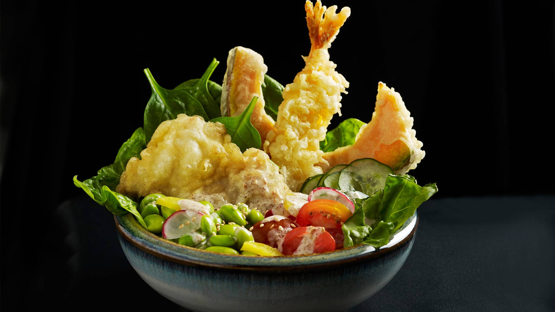 shrimp 桌布 壁紙 — 一個充滿活力的天婦羅碗，金黃色的蝦和蔬菜放在菠菜上，背景為深色。