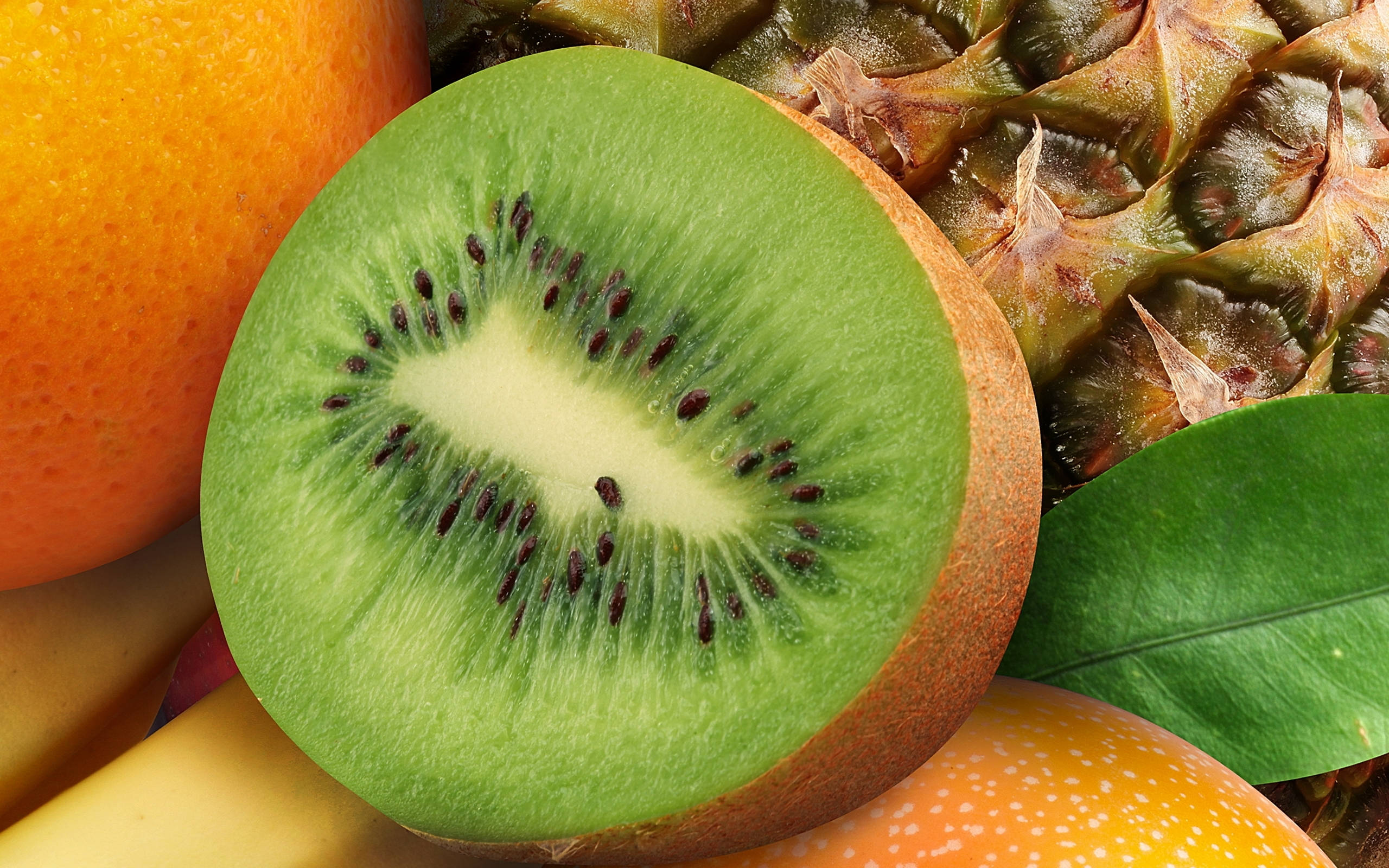 Fruits 桌布 壁紙 — 一個充滿活力的奇異果切片特寫，展現其綠色果肉和黑色種子，旁邊放著橙色的鳳梨和香蕉。