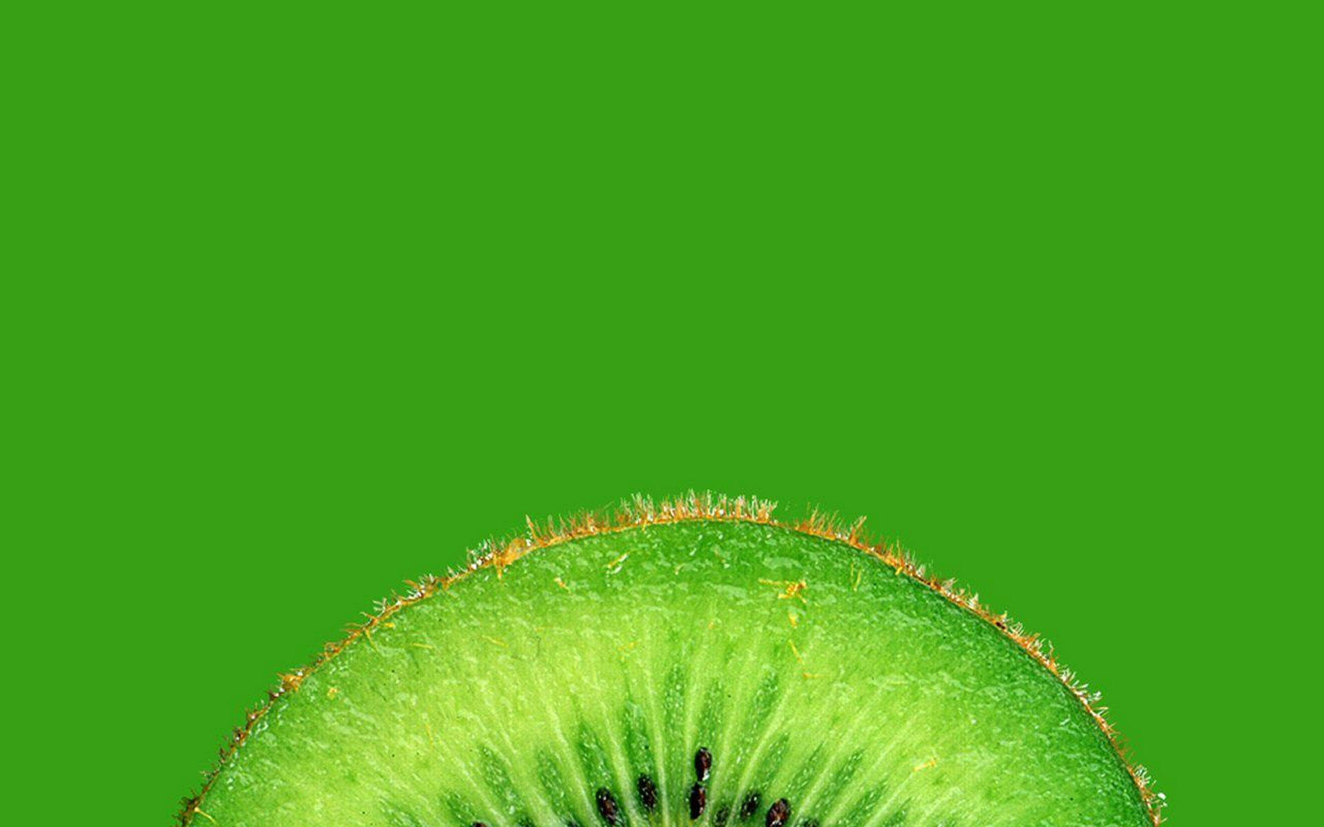 Fruit 桌布 壁紙 — 一個充滿活力的奇異果半邊特寫，展現多汁的綠色果肉和絨毛狀的棕色果皮，背景為純綠色。