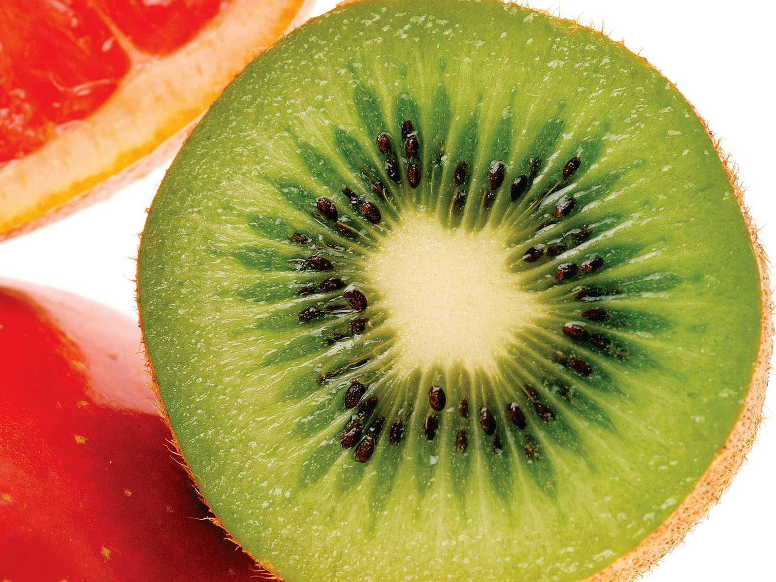Fruit 桌布 壁紙 — 一個充滿活力的奇異果橫切面，黑色種子從淡色中心向外輻射，旁邊有紅西柚片和草莓。