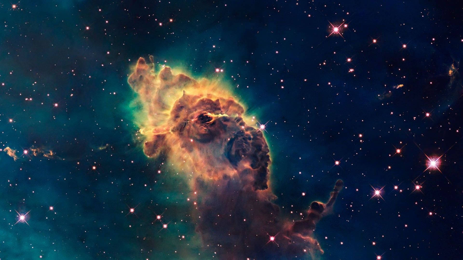 銀河 桌布 壁紙 — 一個充滿活力的宇宙星雲，在繁星點點的深藍色夜空中散發著火橙色和藍綠色的光芒。