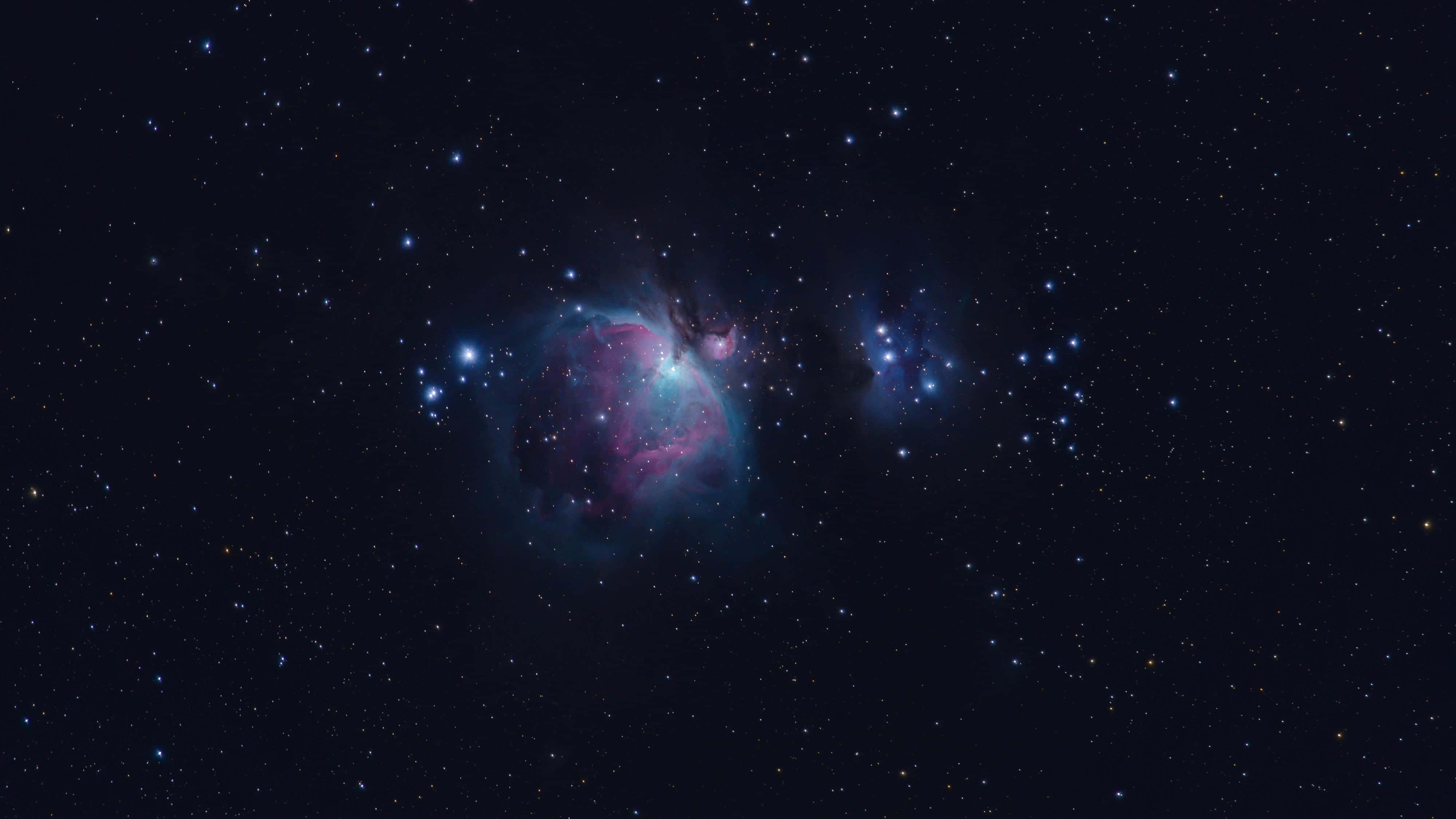 Orion 桌布 壁紙 — 一個充滿活力的宇宙星雲在深空的星場中散發出粉紅色和藍綠色的光芒。