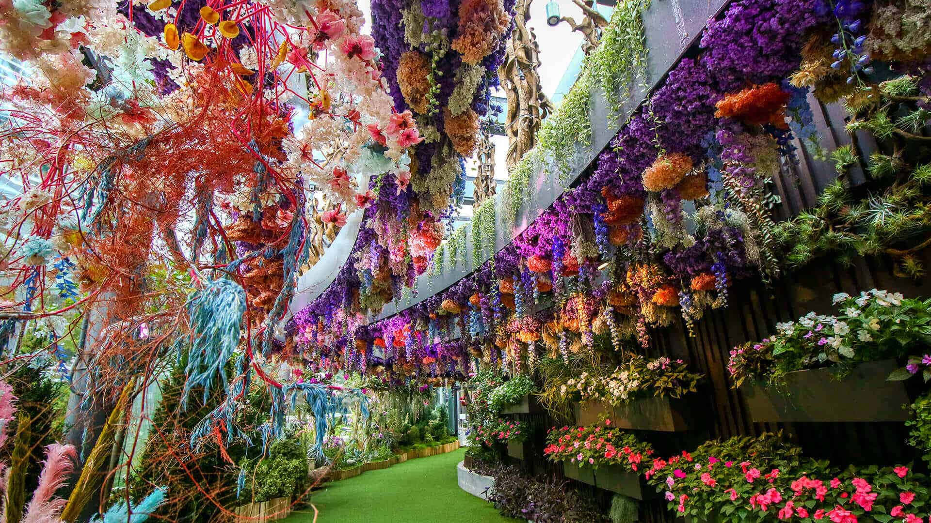 Botanical Garden 桌布 壁紙 — 一個充滿活力的室內花園，在玻璃天花板下，色彩繽紛的花朵和樹葉如瀑布般沿著綠色小徑排列。