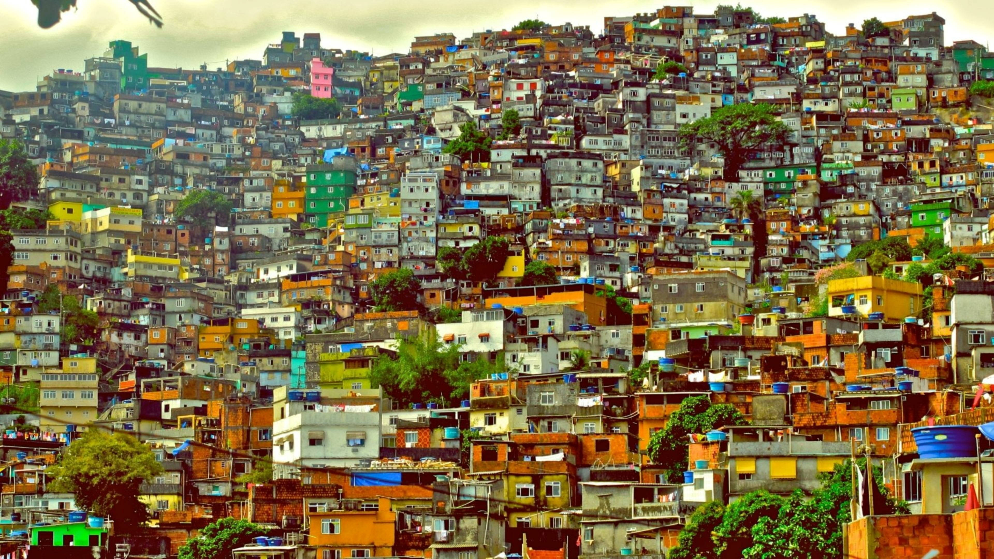 rio 桌布 壁紙 — 一個充滿活力的山坡城市景觀，佈滿色彩繽紛、緊密相連的房屋，天空多雲。