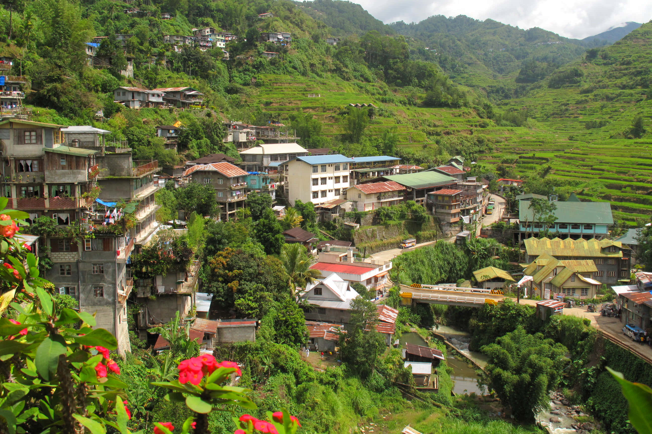 山景 桌布 壁紙 — 一個充滿活力的山坡村莊，色彩繽紛的房屋坐落在鬱鬱蔥蔥的綠色梯田和蜿蜒的河流之間。