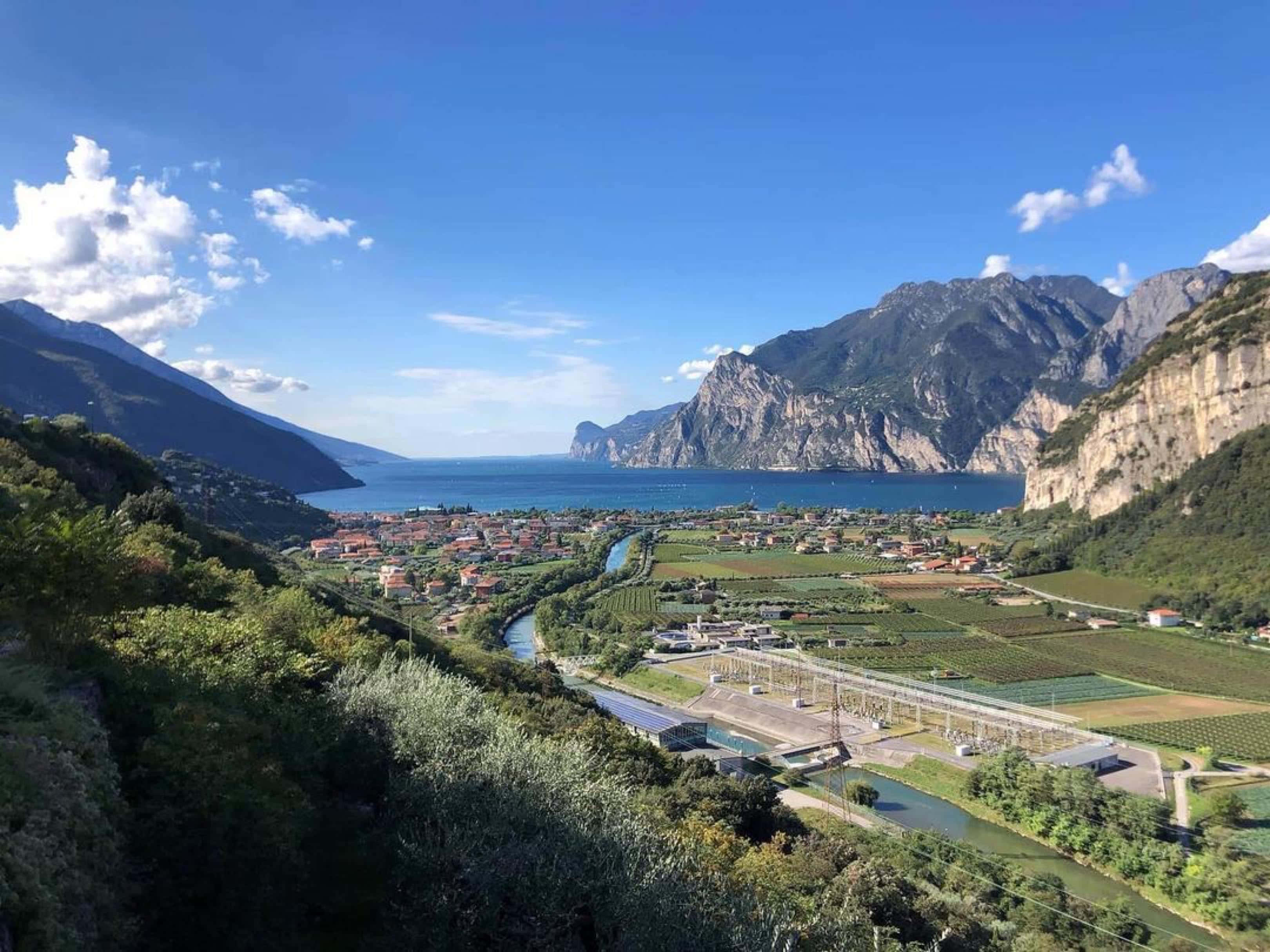 山景 桌布 壁紙 — 一個充滿活力的山谷俯瞰著一個深藍色的湖泊，湖泊坐落在高聳的綠色山脈之間，上方是明亮的藍天和蓬鬆的白雲。
