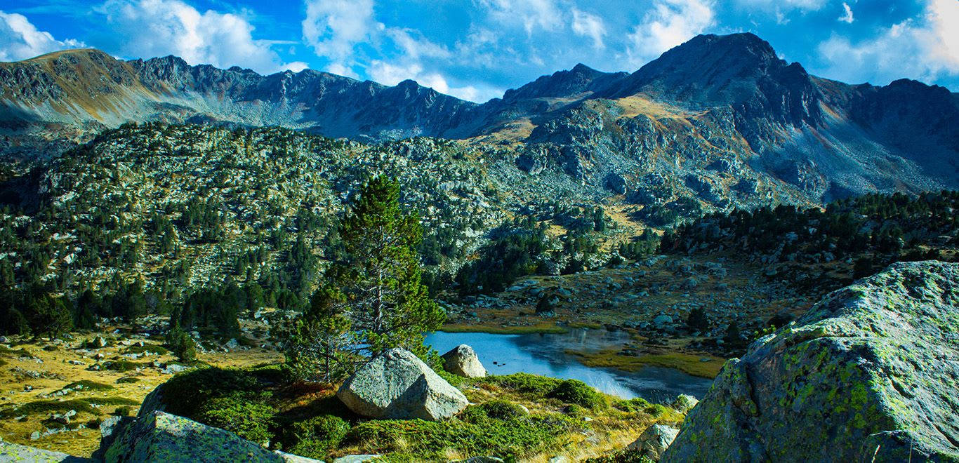 Lake 桌布 壁紙 — 一個充滿活力的山間湖泊，坐落在崎嶇的山峰之間，上方是明亮的藍天和蓬鬆的白雲。