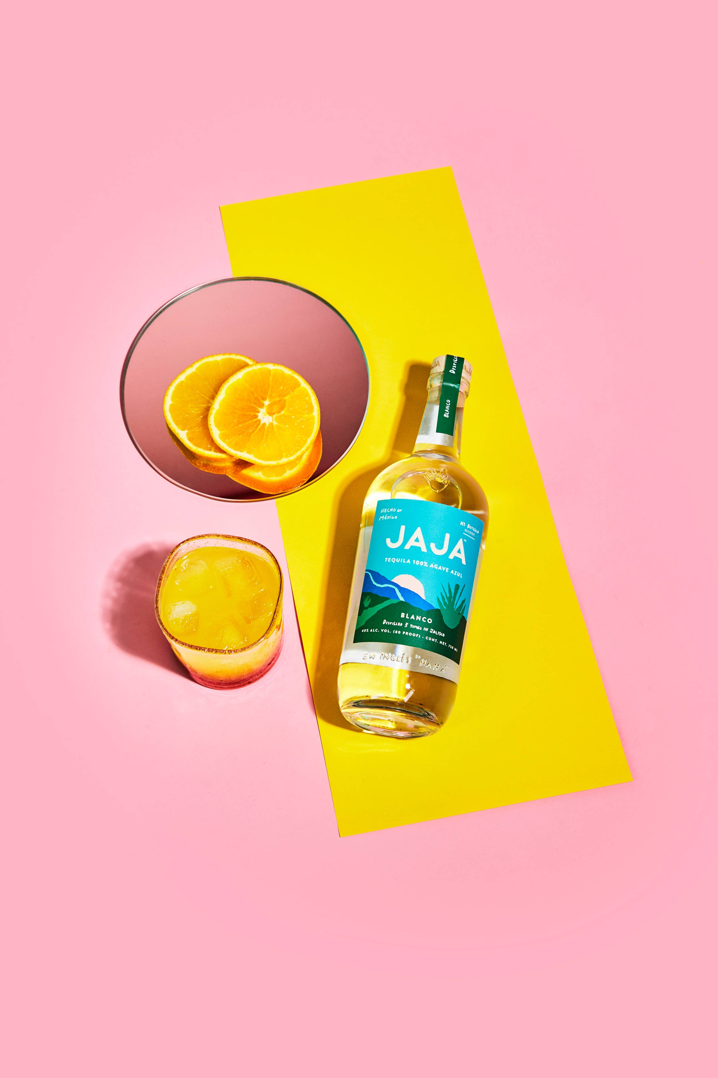 cocktail 桌布 壁紙 — 一個充滿活力的平鋪佈局，包含Jaja龍舌蘭酒瓶、橙片和玻璃杯，背景為粉紅色和黃色。