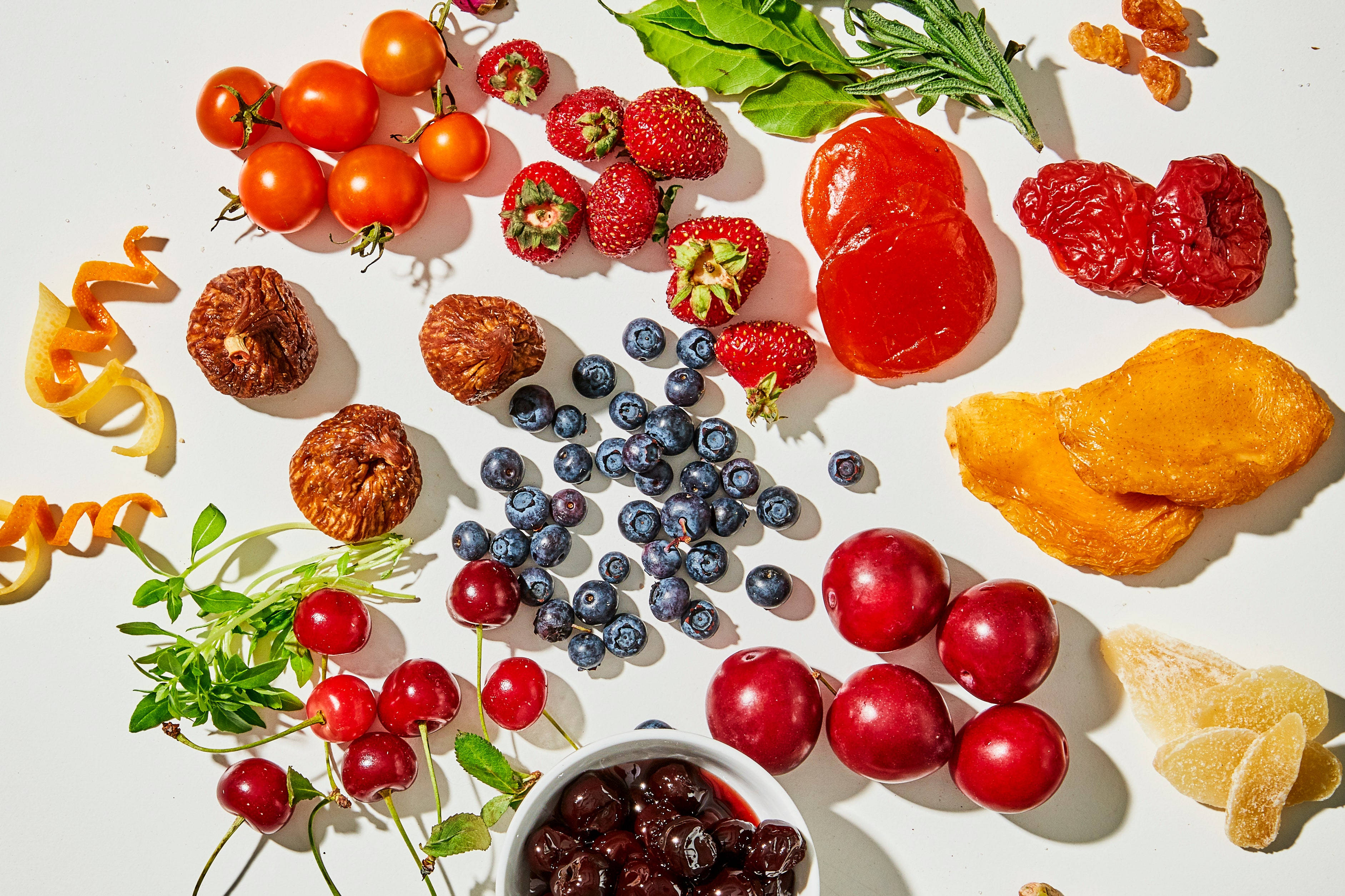 Fruit 桌布 壁紙 — 一個充滿活力的平鋪擺拍，新鮮和乾燥的水果如草莓、藍莓、櫻桃和芒果片排列在明亮的白色表面上。