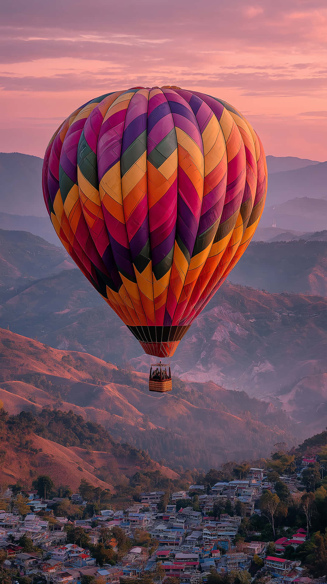 Mountain Balloon Ride 壁紙 — 一個充滿活力的彩色熱氣球漂浮在日落時分的山谷上方，下方有一個小鎮。